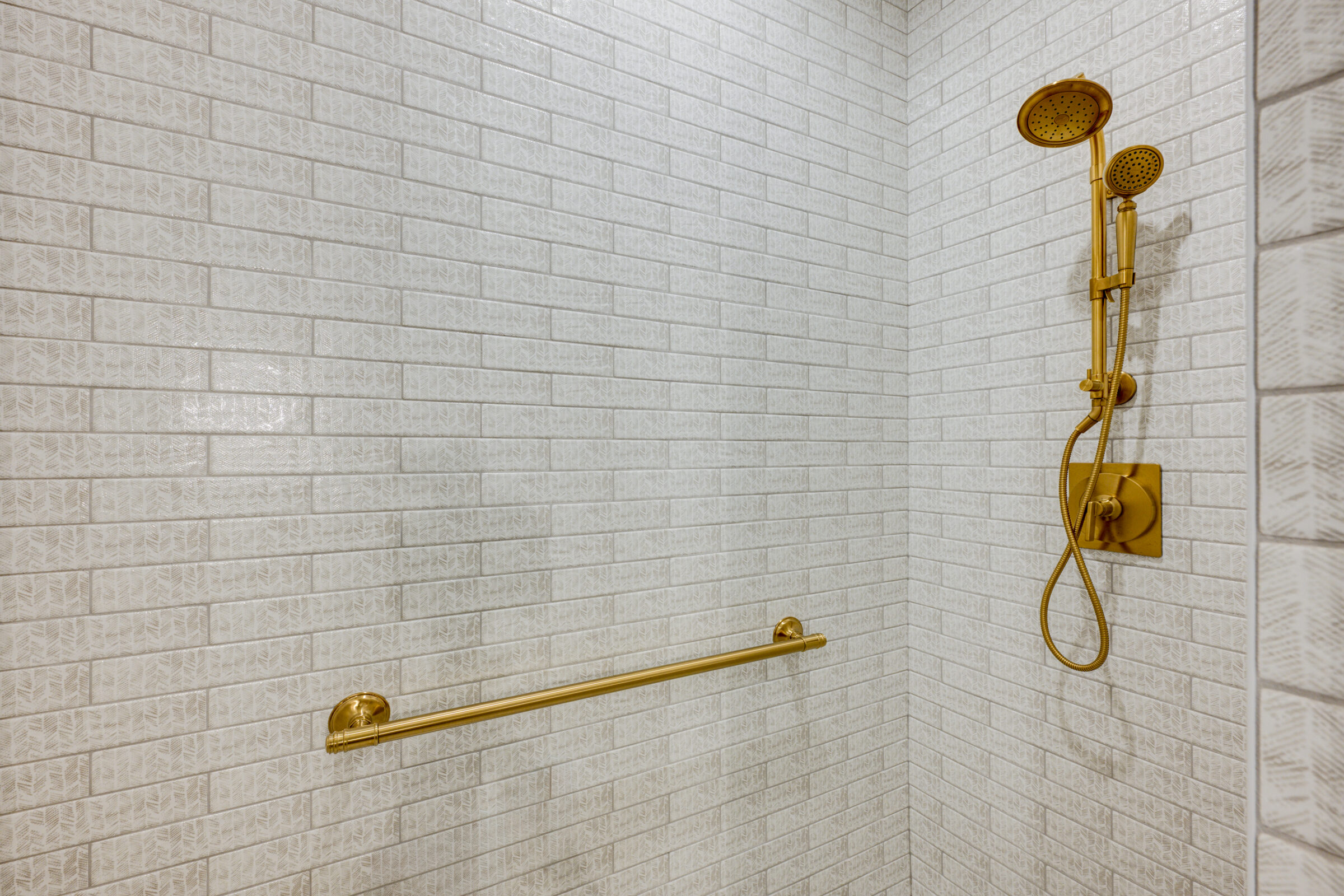 Gold shower fixtures and towel bar on white subway tile wall.
