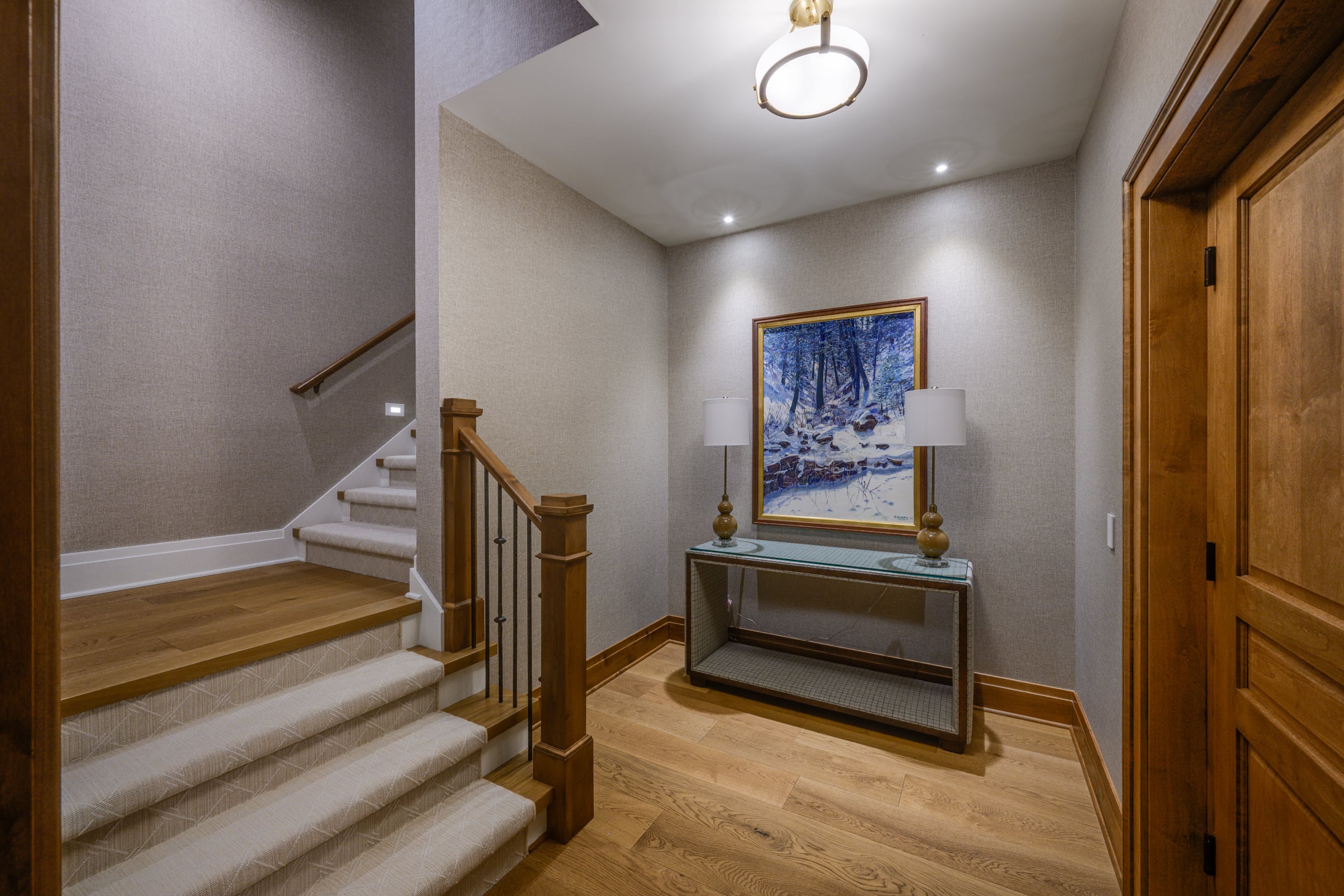 Carpeted stairs, wood accents, and a winter forest painting in a hallway.
