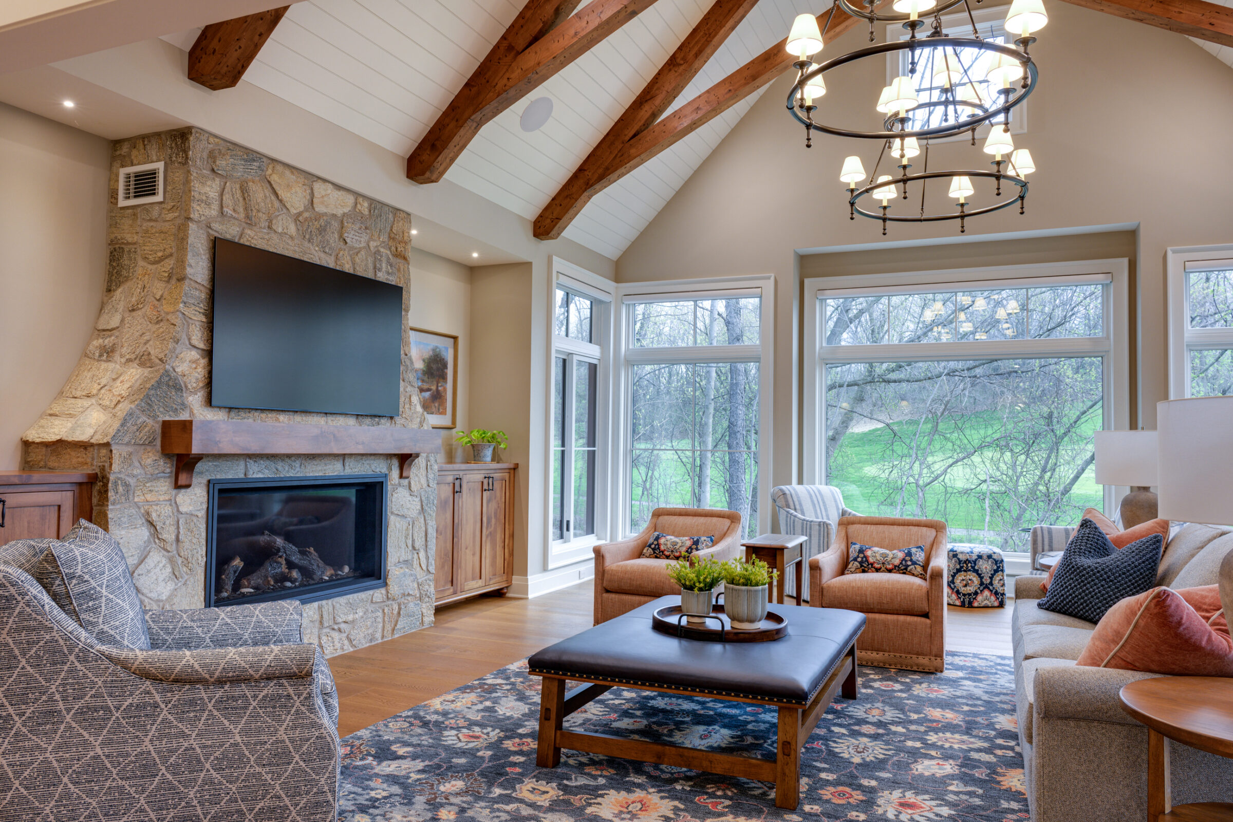 Living room with stone fireplace, large windows, and vaulted beamed ceiling.