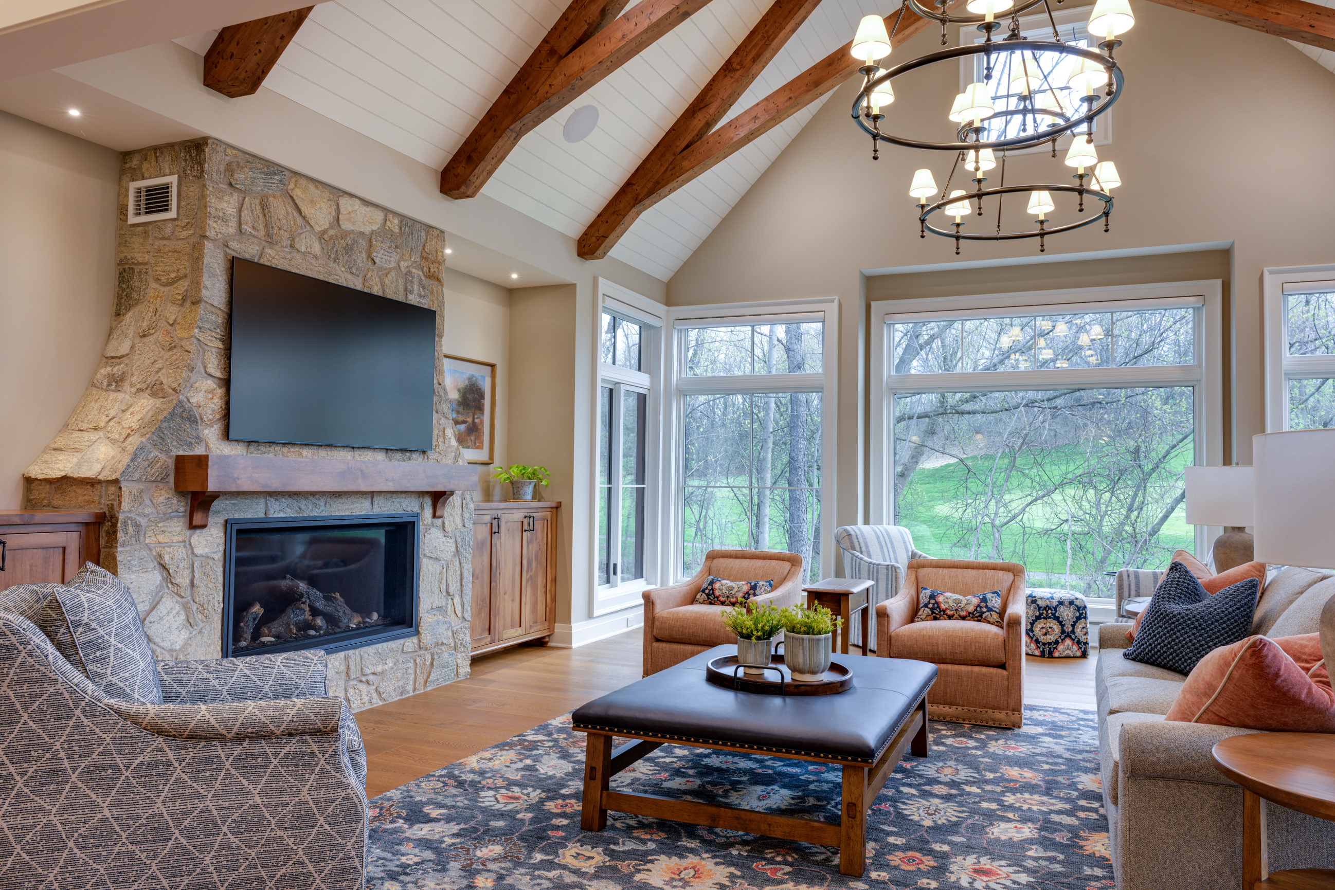 Living room with stone fireplace, large windows, and vaulted beamed ceiling.