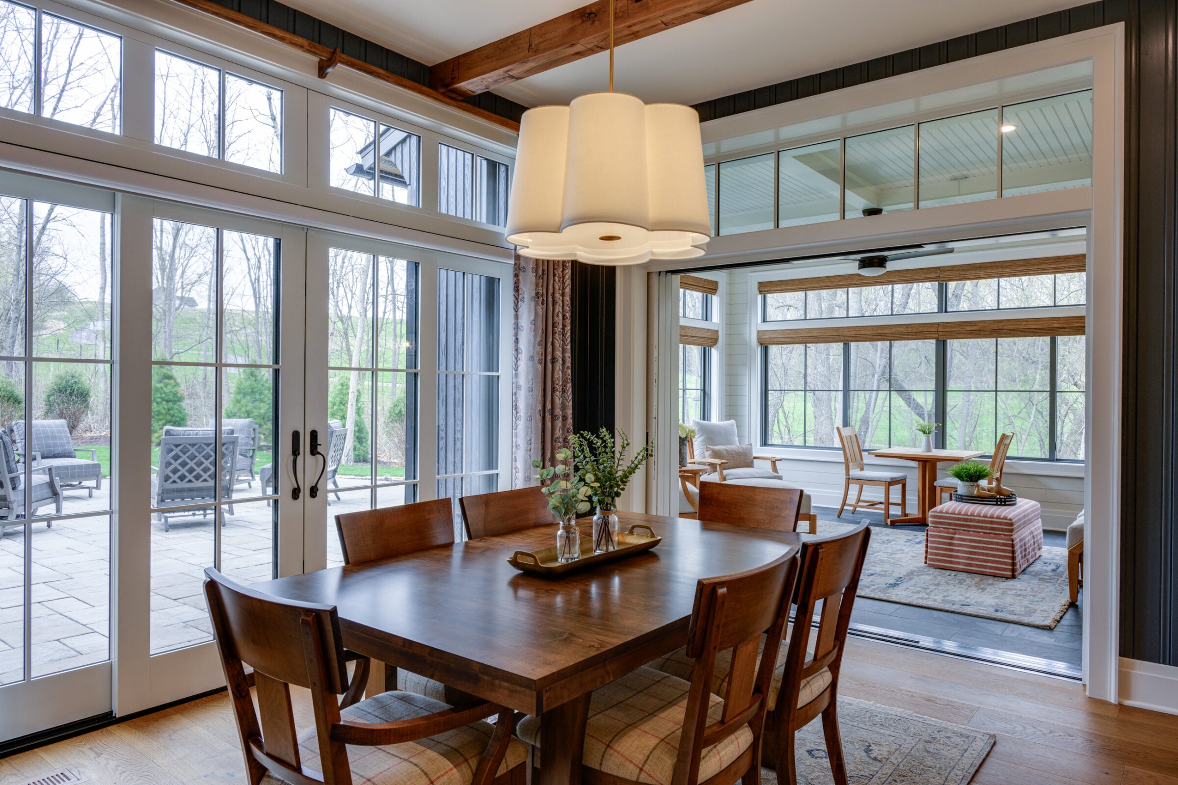 Wooden dining table with chairs, large windows, and outdoor patio view.