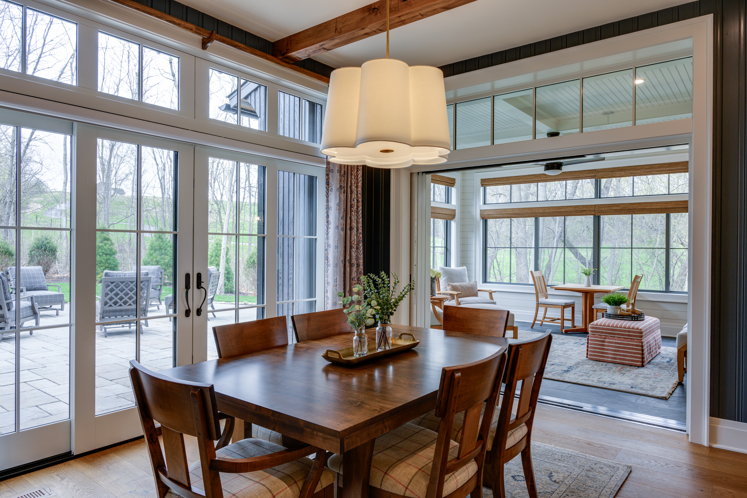 Wooden dining table with chairs, large windows, and outdoor patio view.