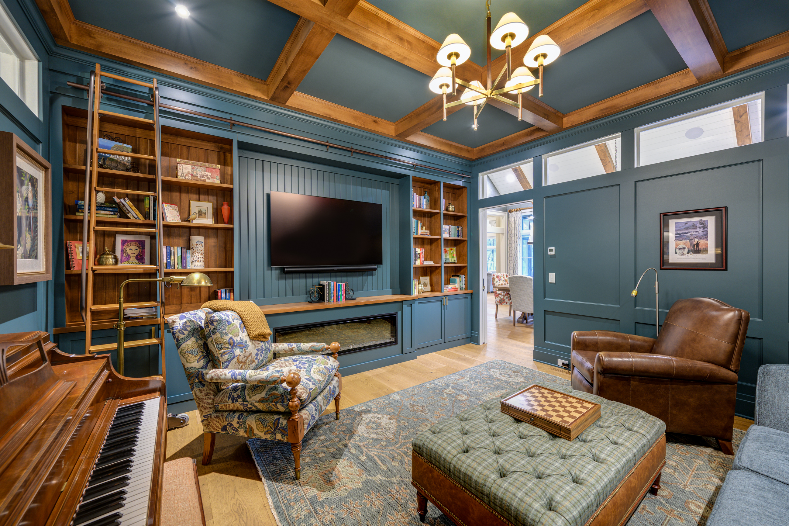 Cozy library with built-in bookshelves, fireplace, piano, and plush seating.