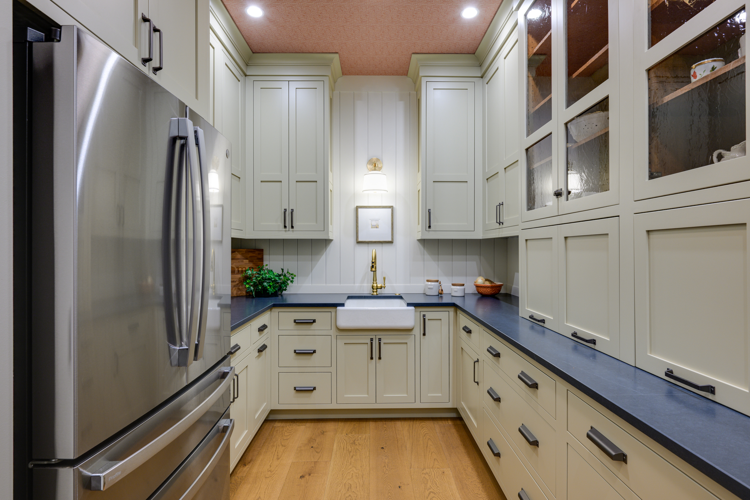 Stainless steel refrigerator and cream-colored cabinets with a farmhouse sink and brass faucet.