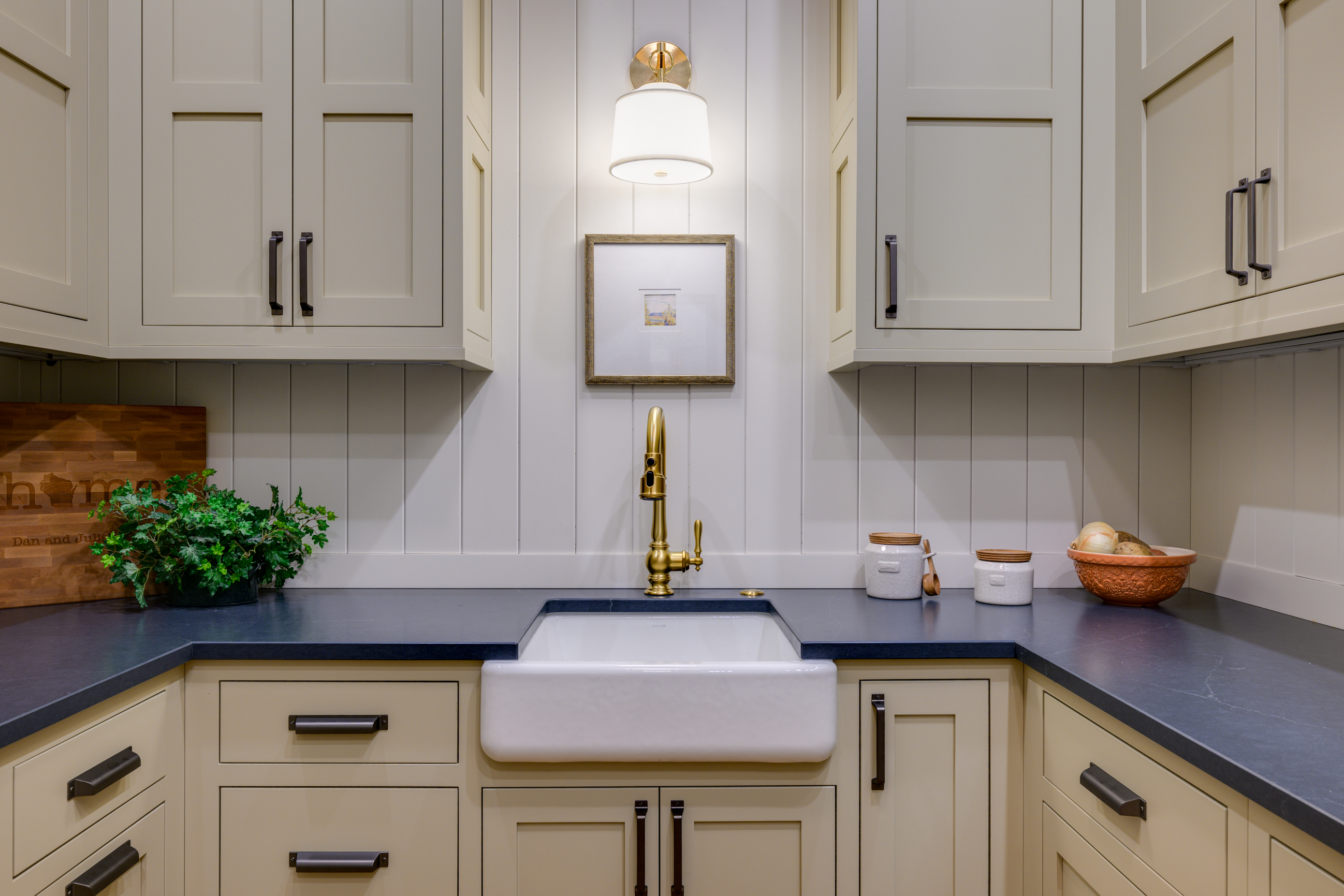 Farmhouse sink with brass faucet, light cabinets, and dark countertop.