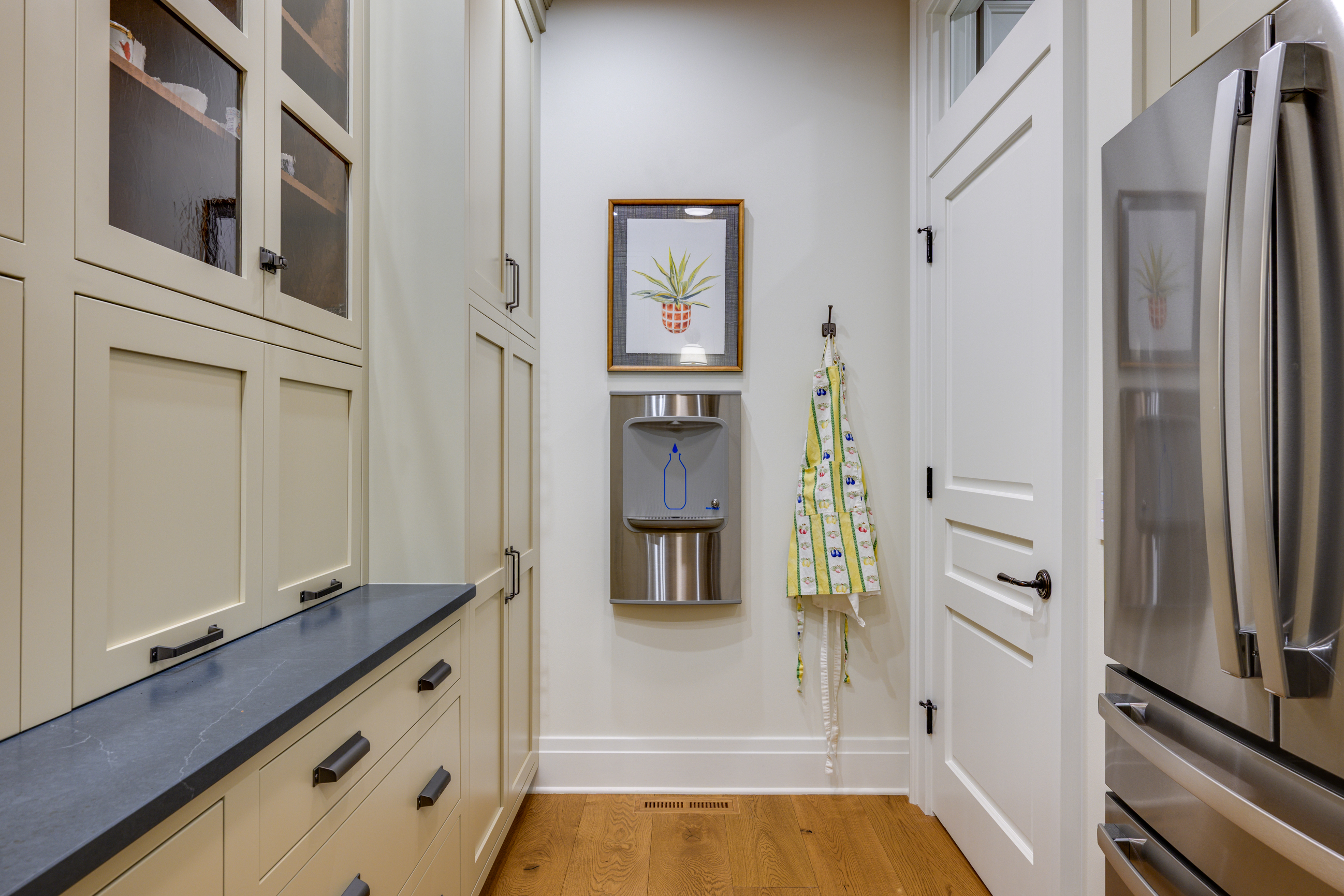 Kitchen pantry with cabinets, water cooler, framed pineapple art, and refrigerator.