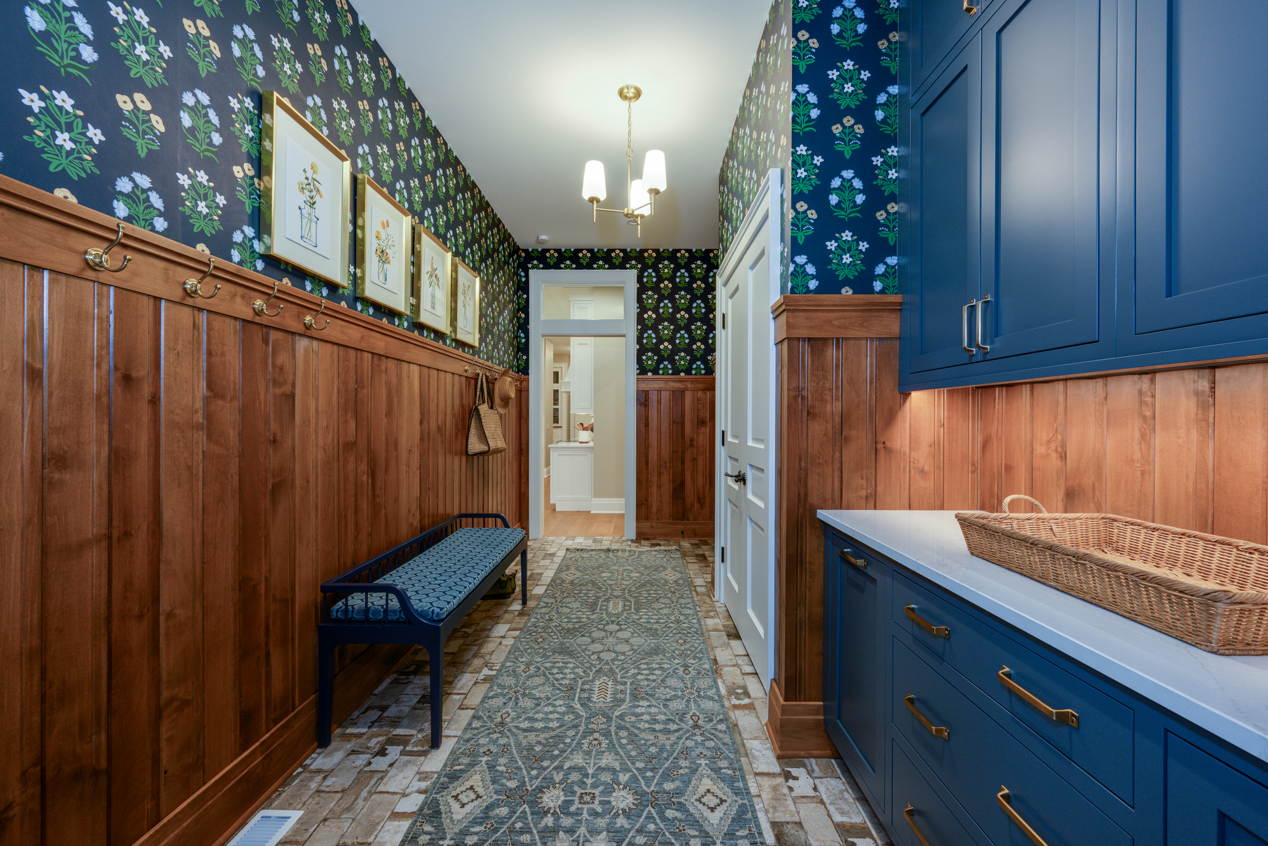 Hallway with floral wallpaper, wood paneling, blue bench, and navy cabinets.