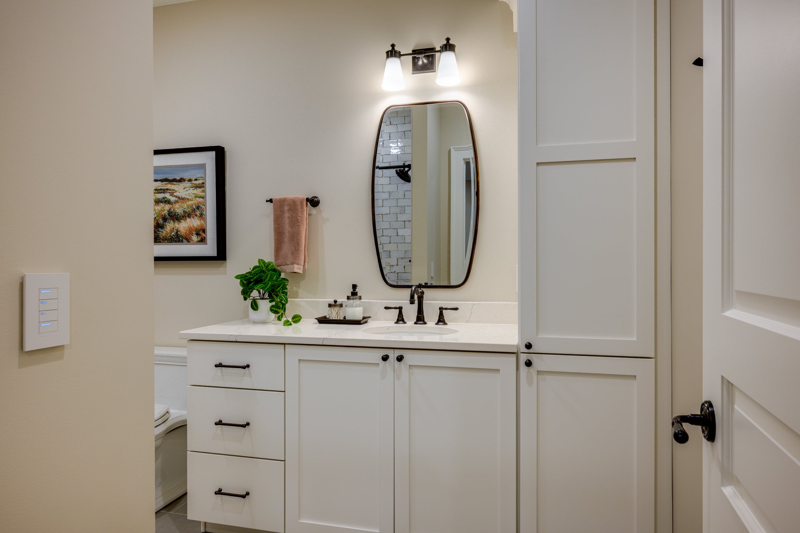 Modern bathroom vanity with white cabinets, black hardware, and a large oval mirror.