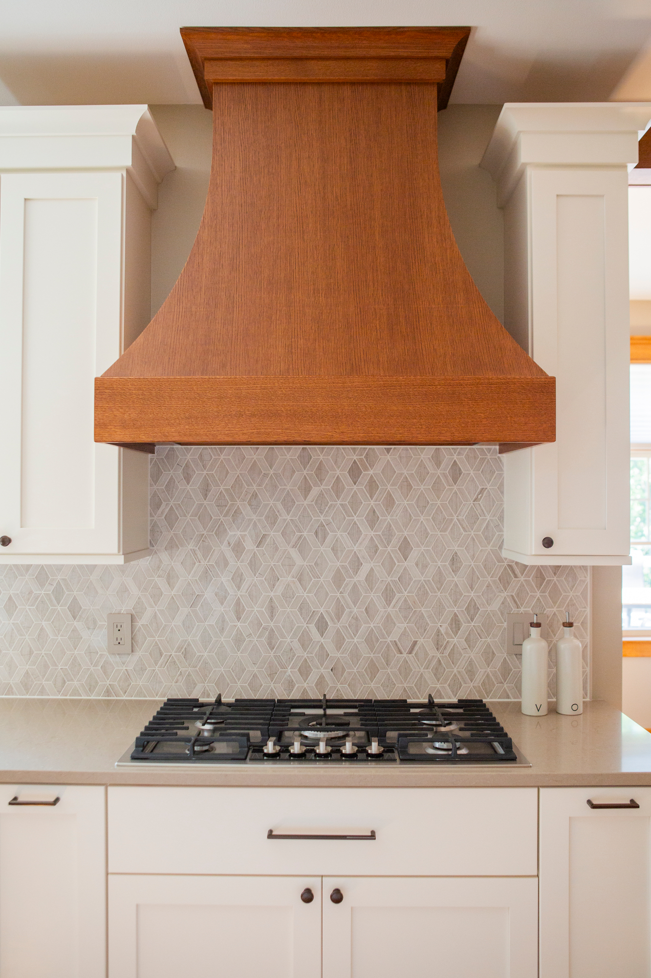 Wooden range hood over a gas stove with a diamond-patterned backsplash.