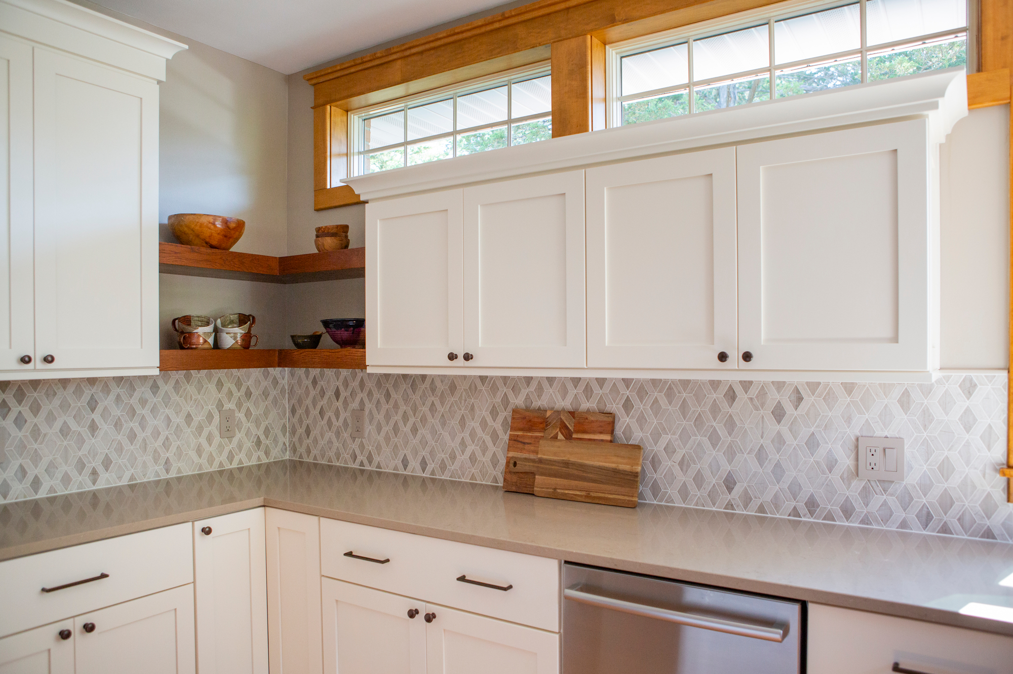 White kitchen cabinets, diamond tile backsplash, and wooden shelves with bowls.