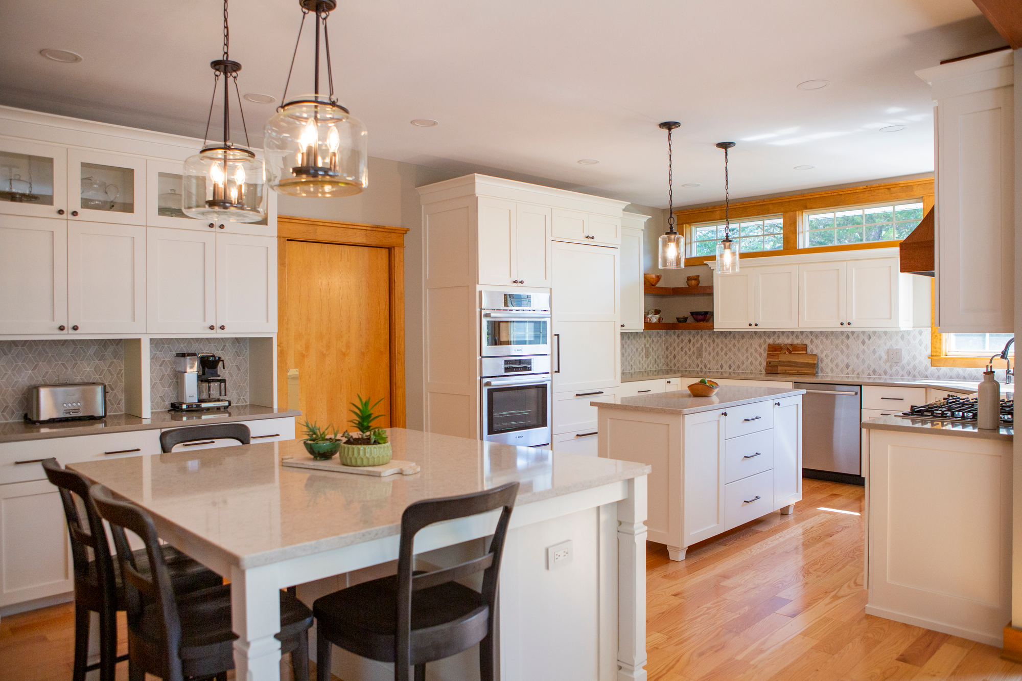 Modern white kitchen with island, pendant lights, and stainless steel appliances.