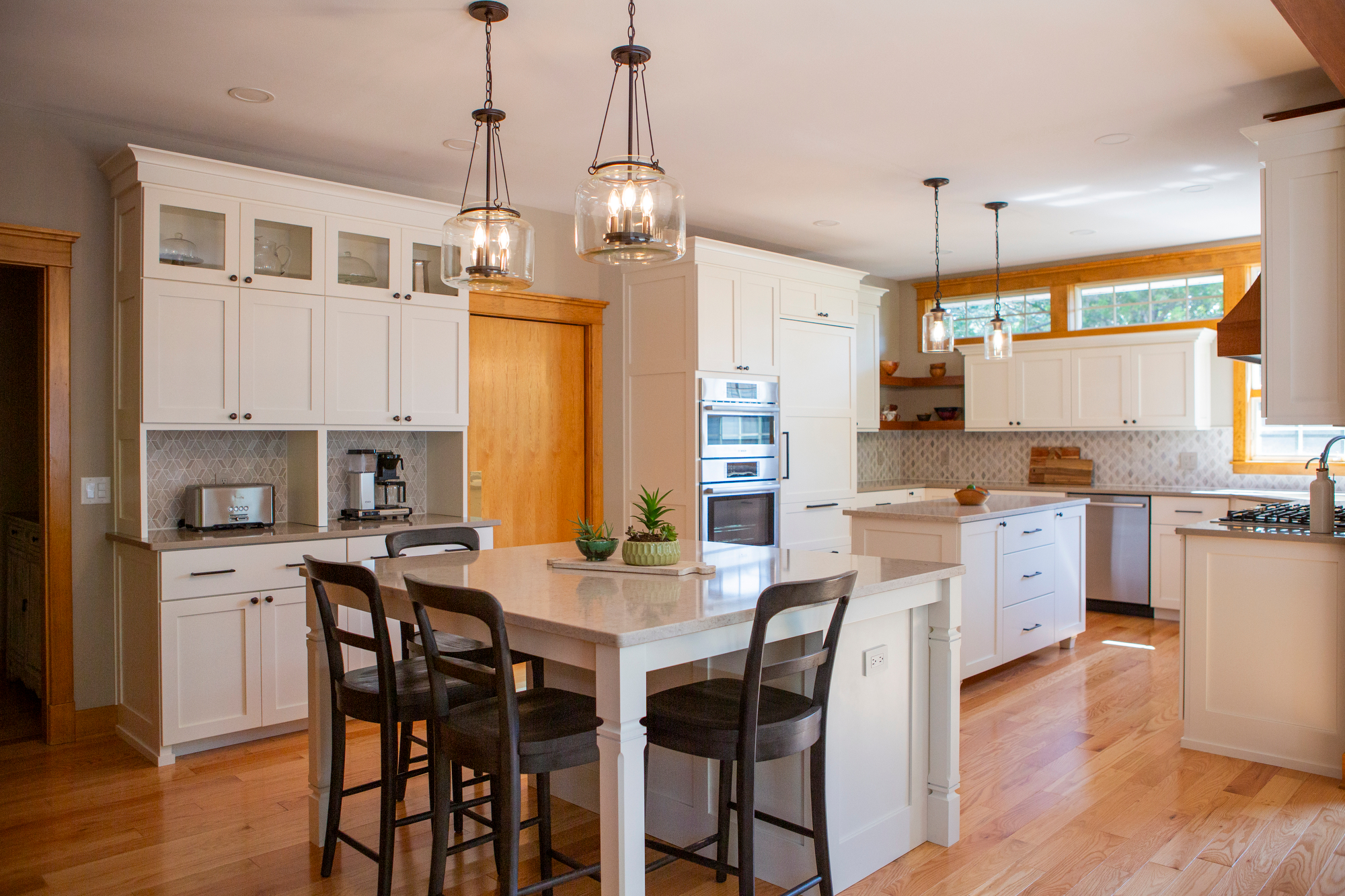 Modern white kitchen with island, pendant lights, and stainless steel appliances.