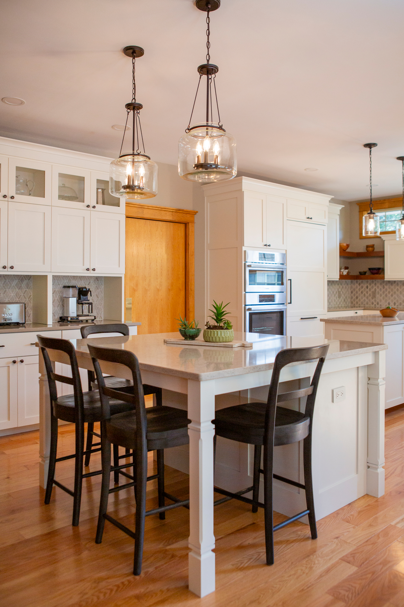 Kitchen island with bar stools, white cabinets, and pendant lights.
