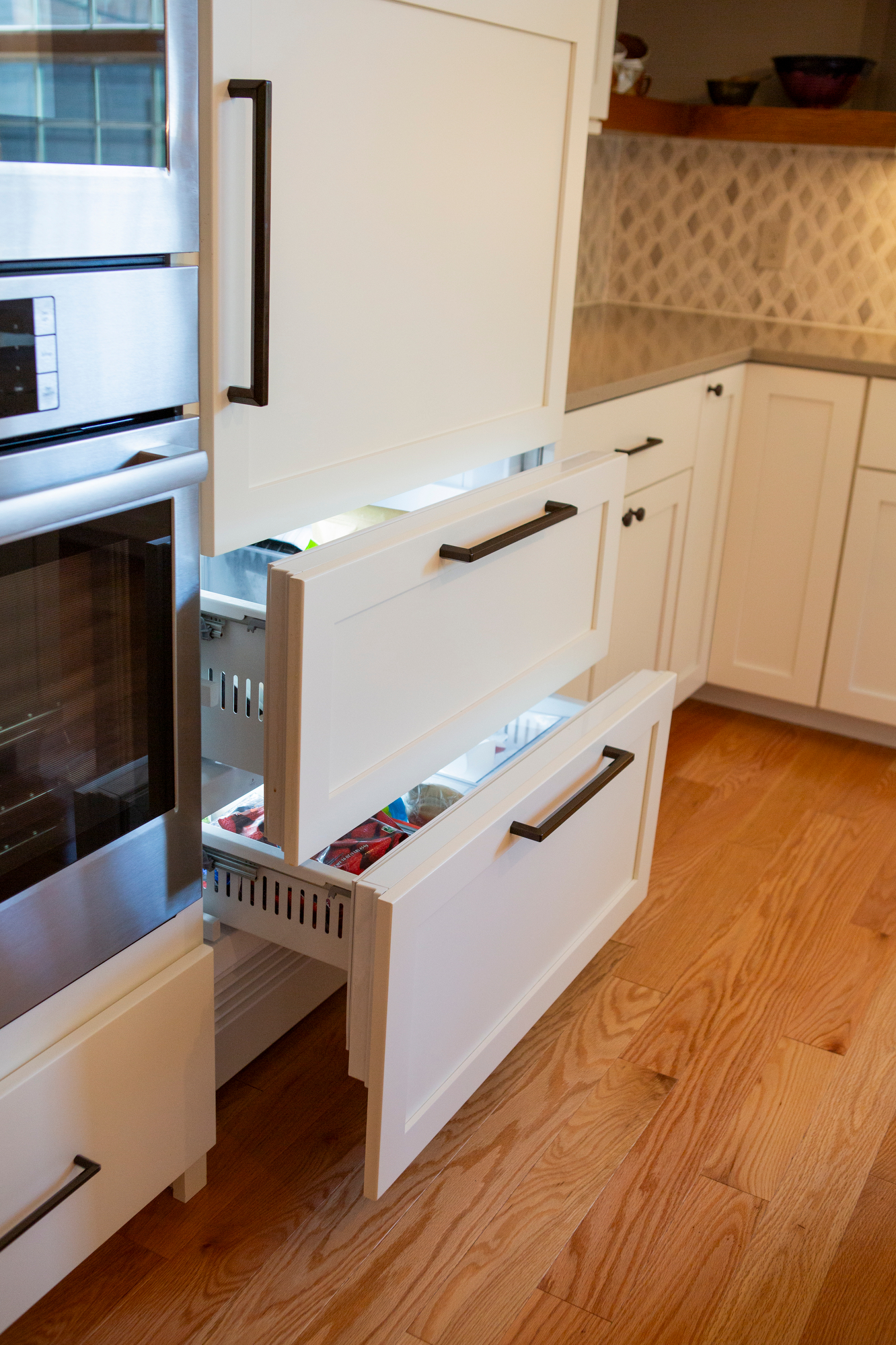 White refrigerator drawers open, revealing contents and a built-in oven.