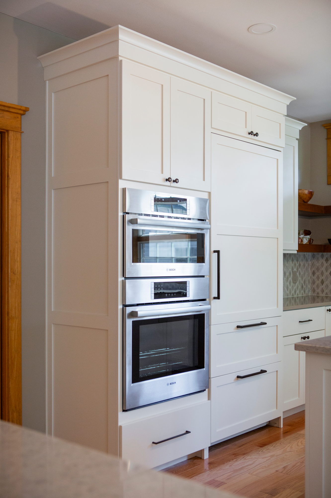 Stacked stainless steel ovens integrated into white kitchen cabinetry with black handles.