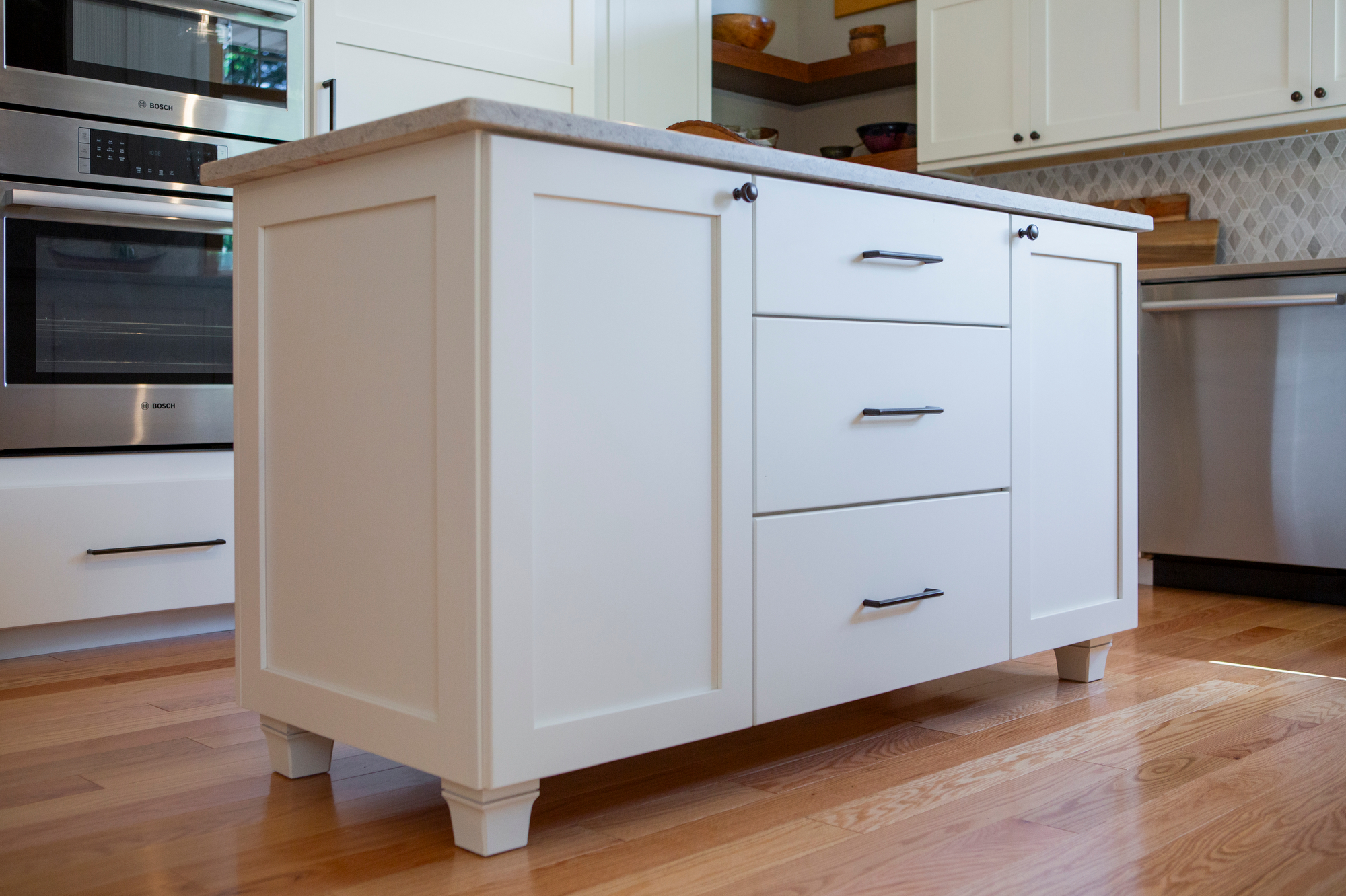 White kitchen island with drawers and a cabinet, next to stainless steel appliances.