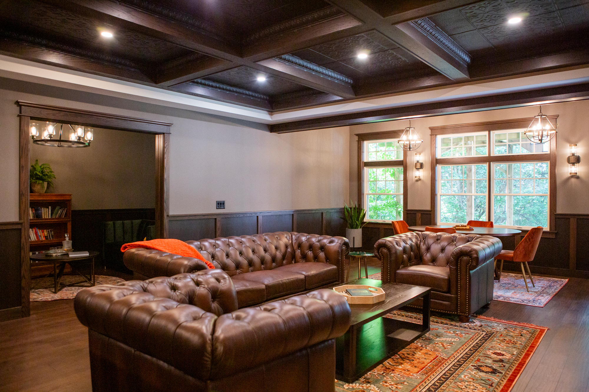 Tufted leather sofas and armchairs in a room with a coffered ceiling and large windows.