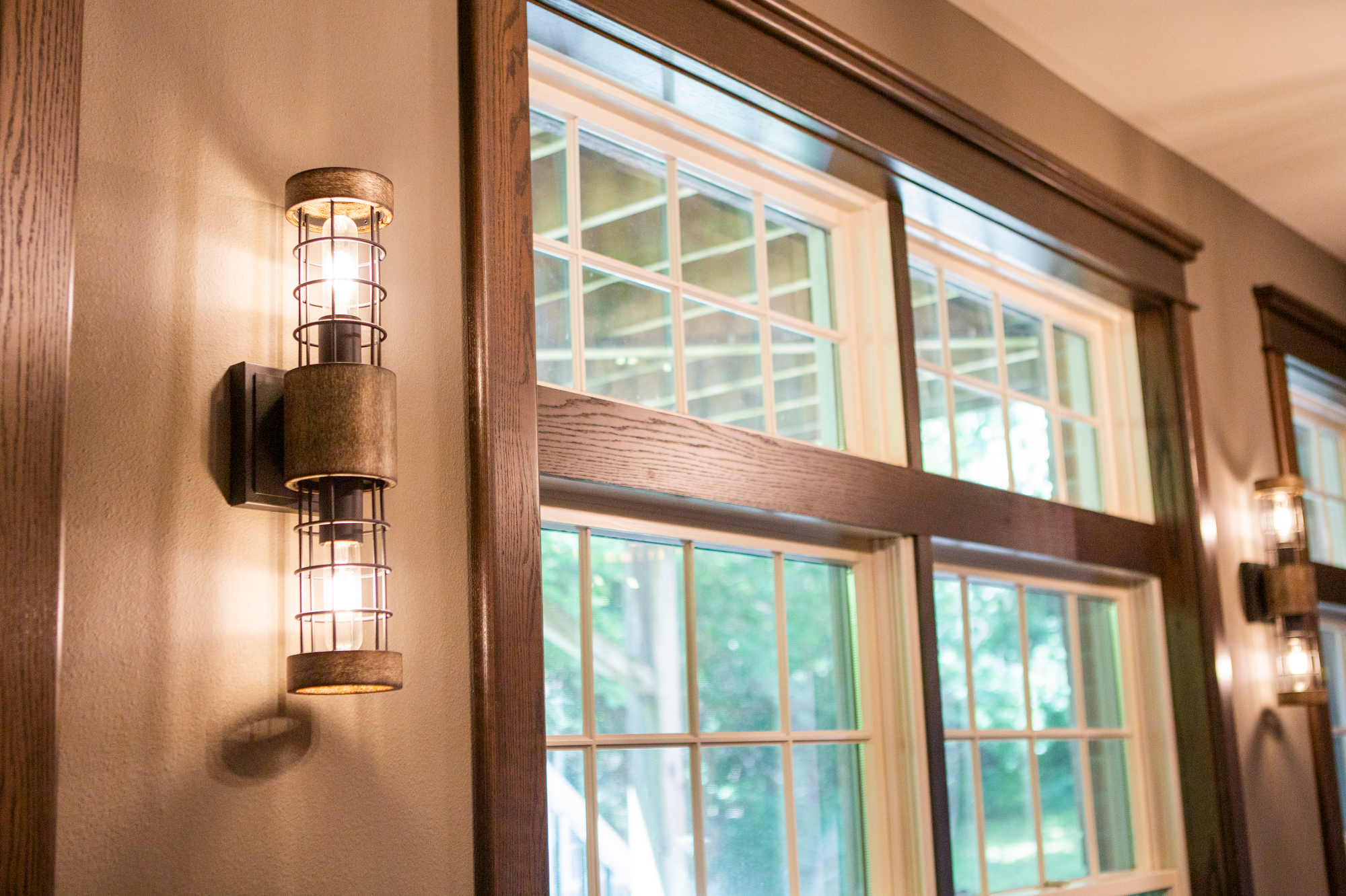 Industrial-style wall sconce with two caged bulbs next to a grid-windowed wall.