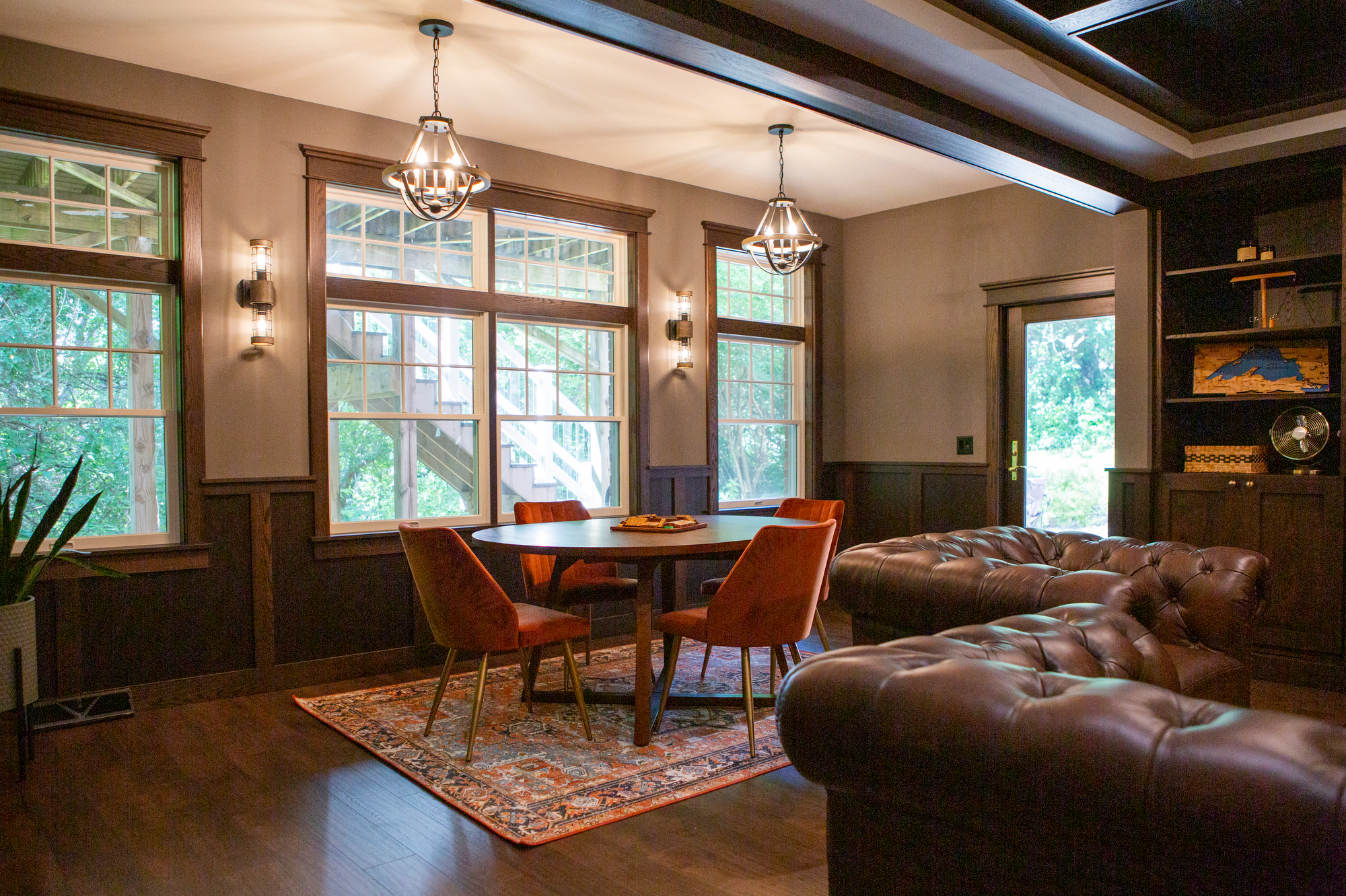 Round table with orange chairs, tufted leather sofas, and large windows.