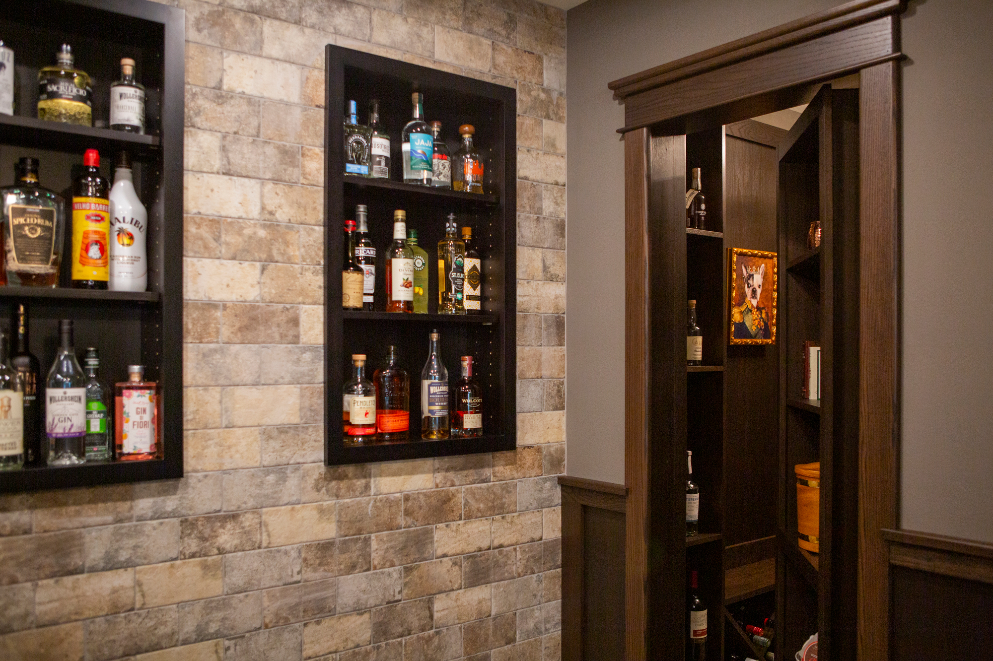 Shelves of liquor bottles and a hidden door bar with a dog portrait.