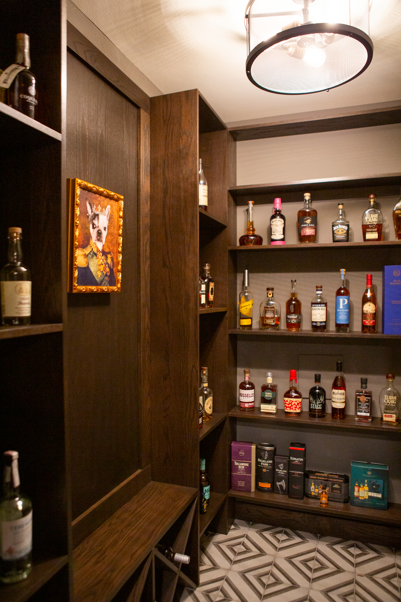 Framed portrait of a dog in a military uniform hangs on a dark wood wall next to shelves of liquor bottles.