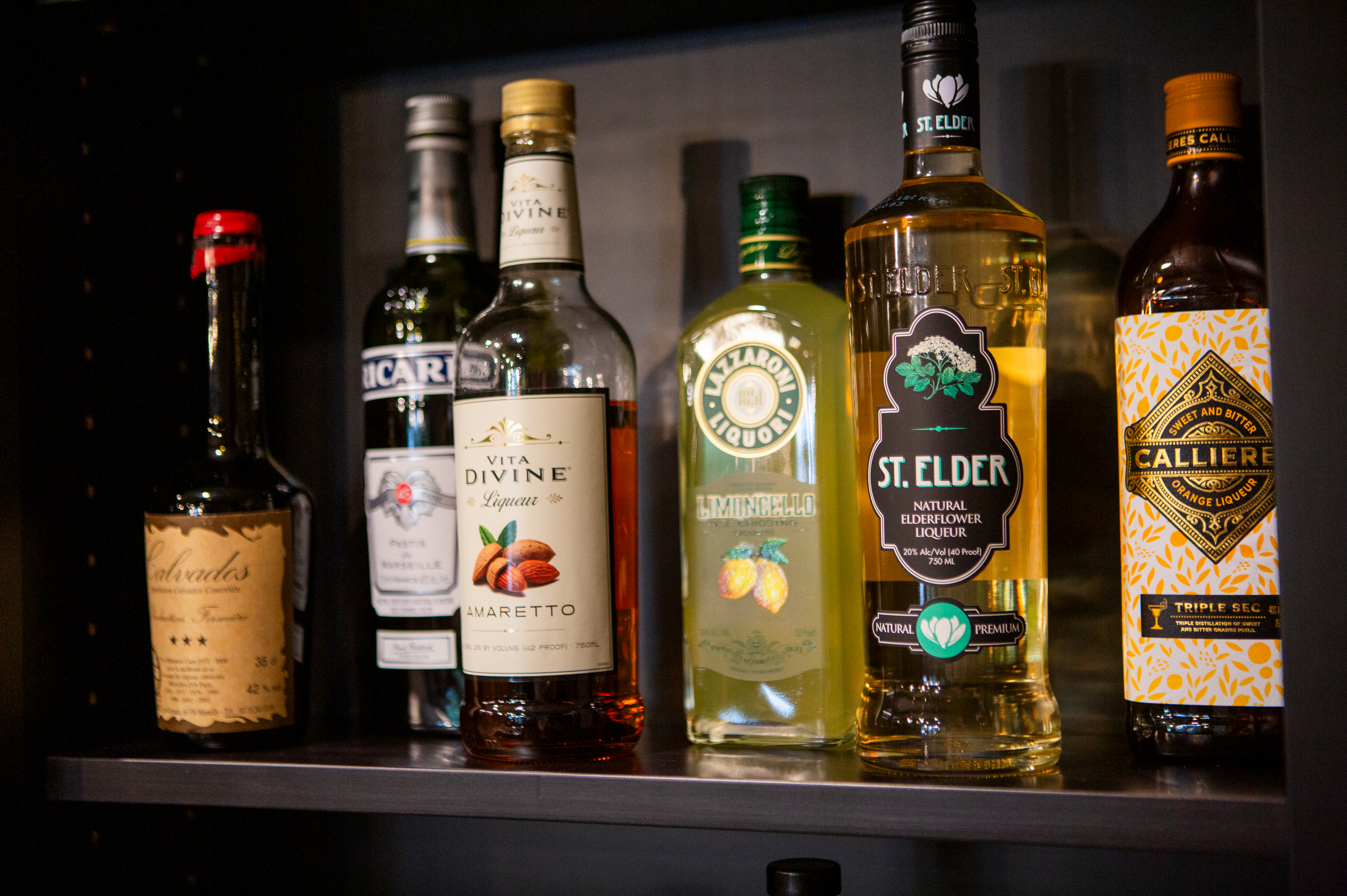 Assortment of liqueurs on a shelf: Calvados, Amaretto, Limoncello, St. Elder, and Calliere Orange.