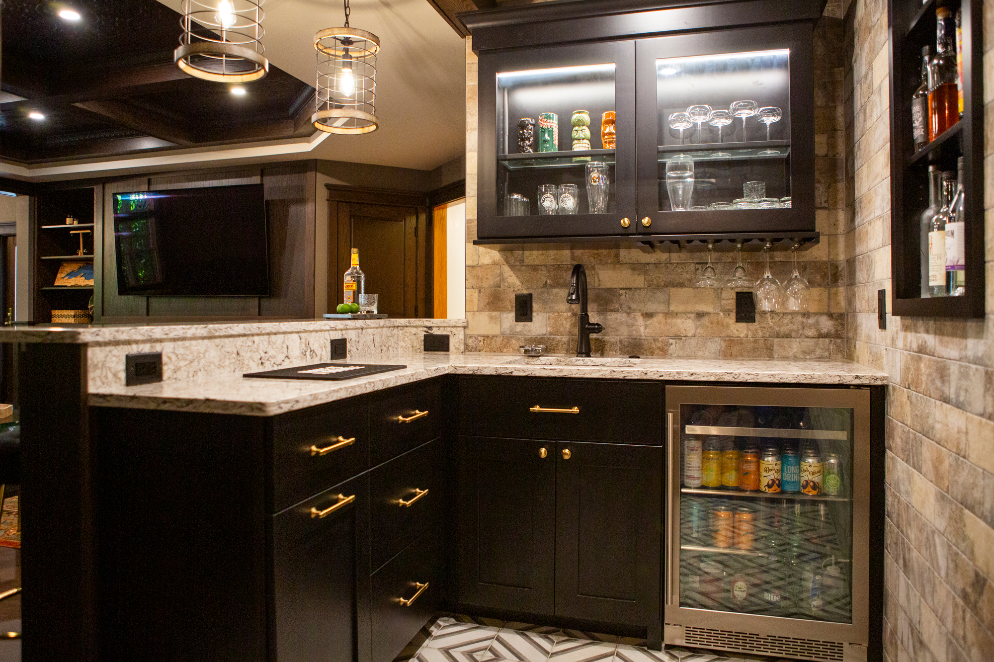 Modern home bar with black cabinets, granite countertop, mini-fridge, and glass-fronted liquor cabinet.