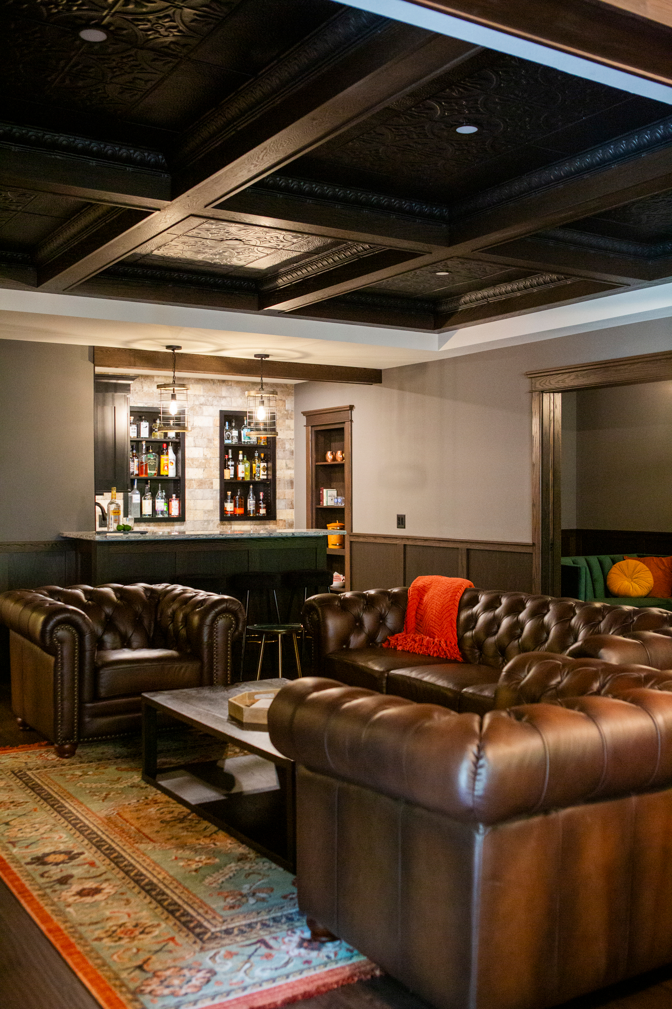 Leather chesterfield sofas and armchairs in a room with a bar and ornate ceiling.