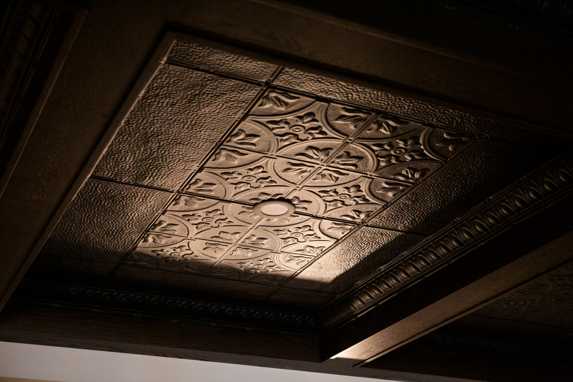 Dark brown embossed tin ceiling tiles with floral patterns and a central light fixture.