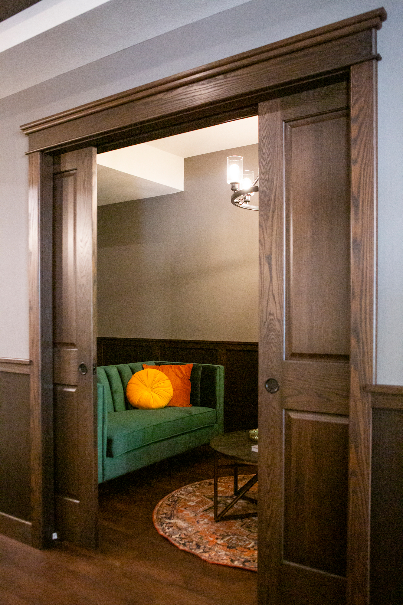 Open wooden sliding doors reveal a green sofa with orange pillows and a round rug.