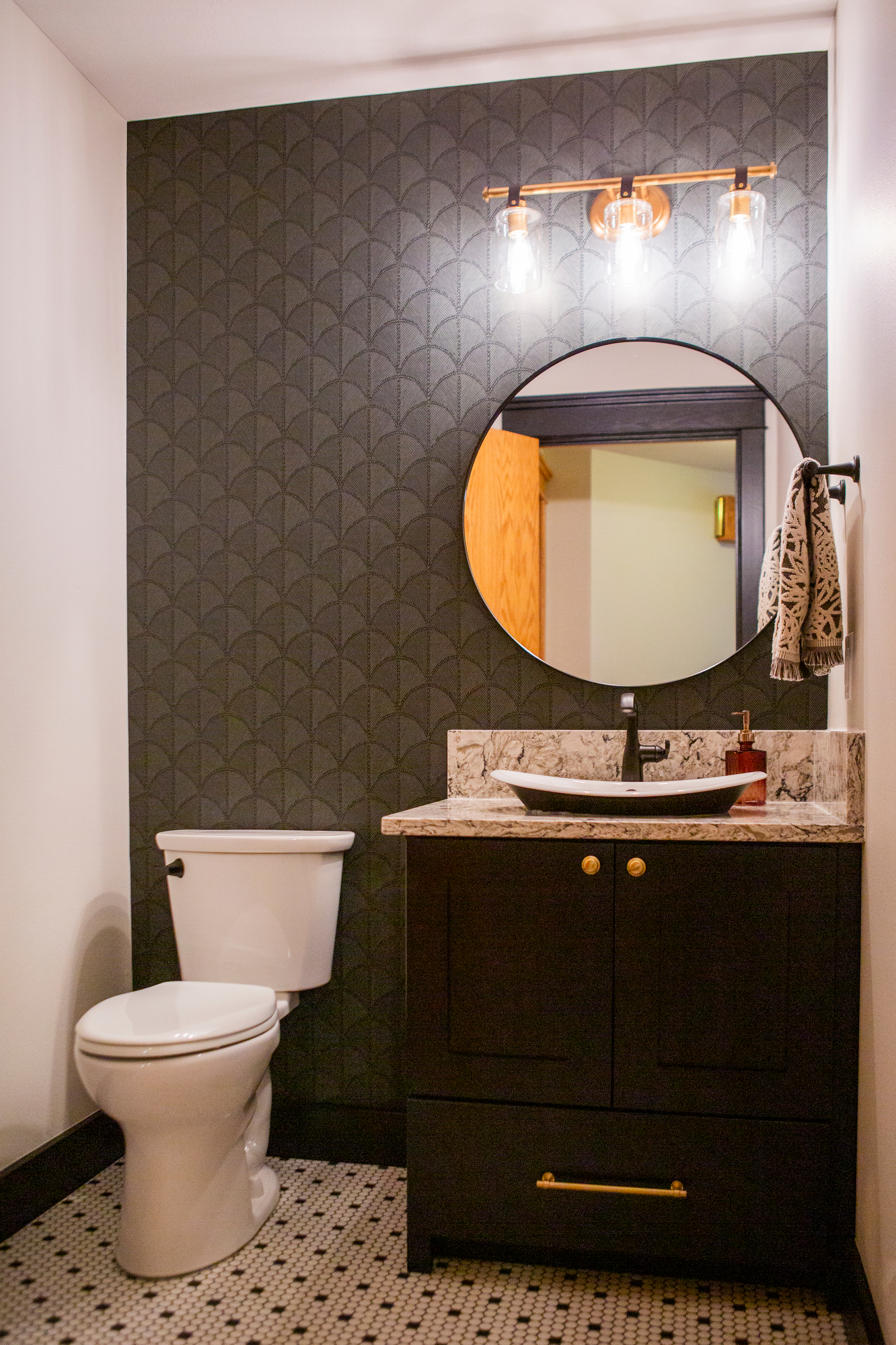 Modern bathroom with dark patterned wallpaper, vanity, toilet, and round mirror.