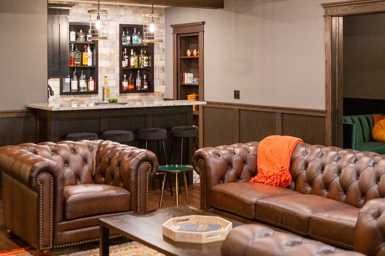 Brown leather tufted sofas and chairs in a home bar area with a well-stocked bar.
