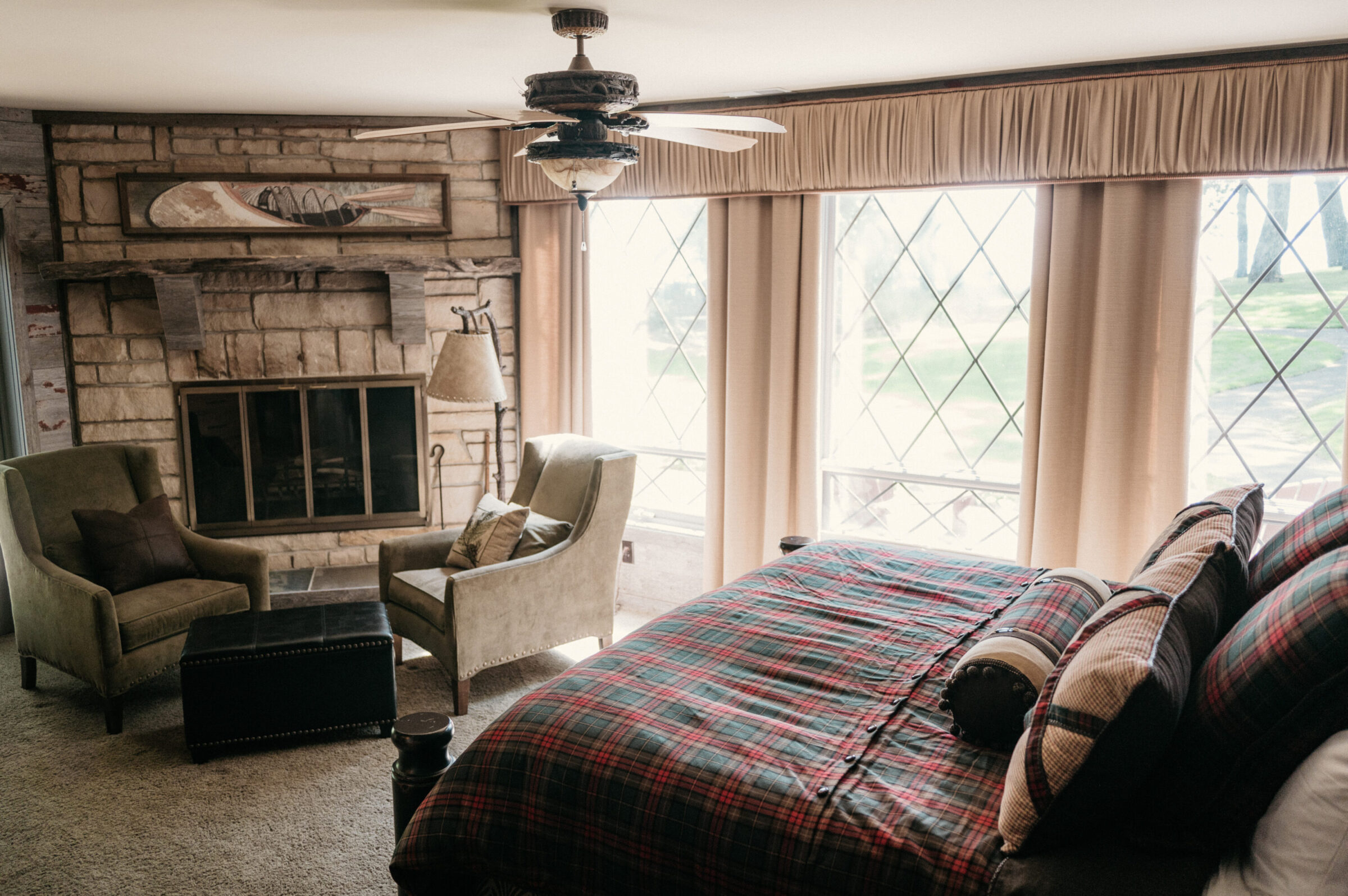 Bedroom with stone fireplace, two chairs, and a plaid bed.