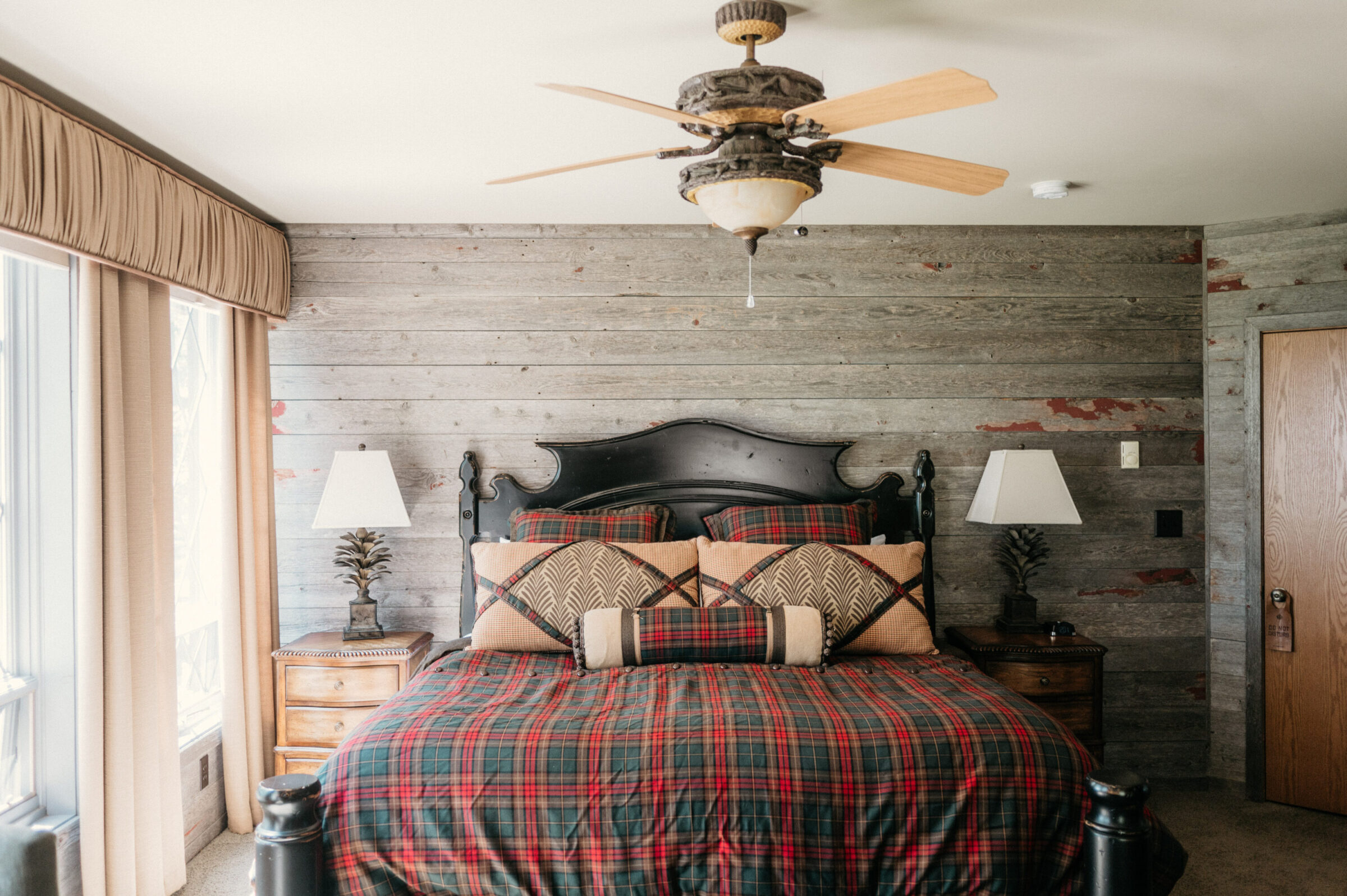 Rustic bedroom with plaid bedding, dark wood headboard, and wood-paneled walls.