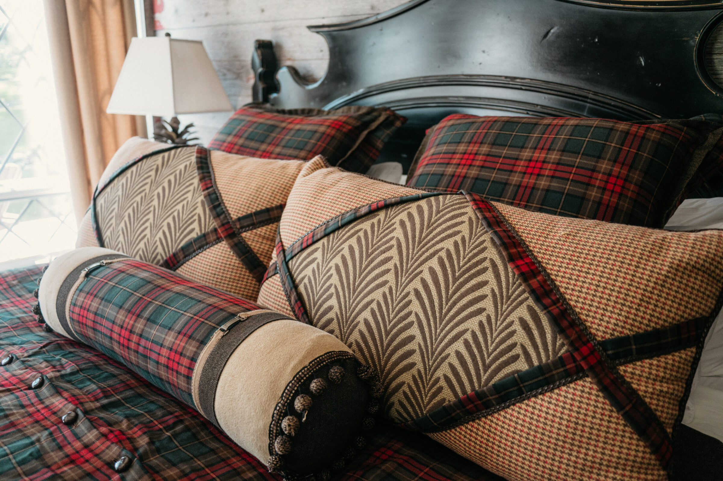 Plaid and patterned pillows on a bed with a dark headboard.