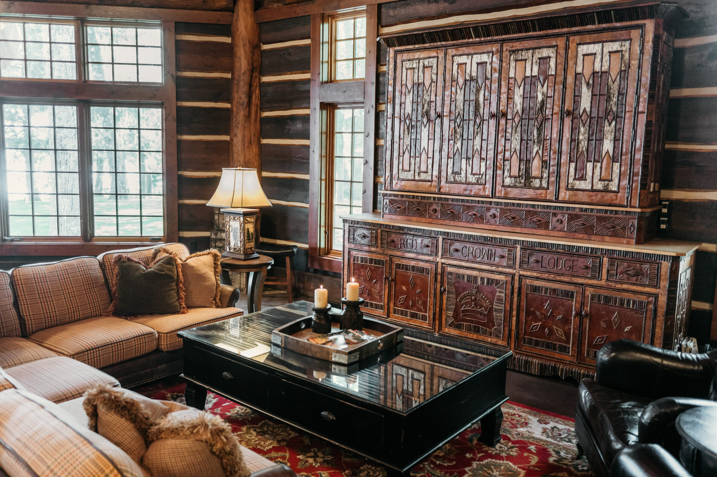 Log cabin living room with plaid sofa, black coffee table, and ornate wooden cabinet.