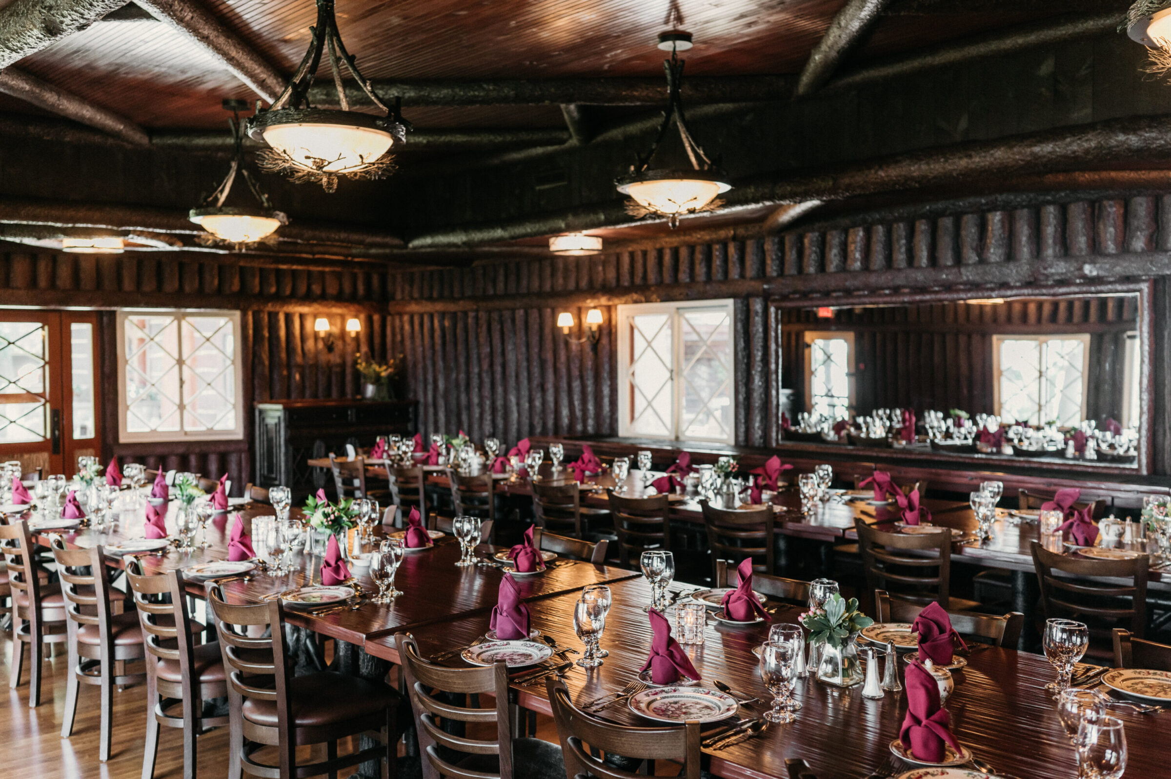 A formal dining room with long tables set for an event, featuring wood paneling and chandeliers.