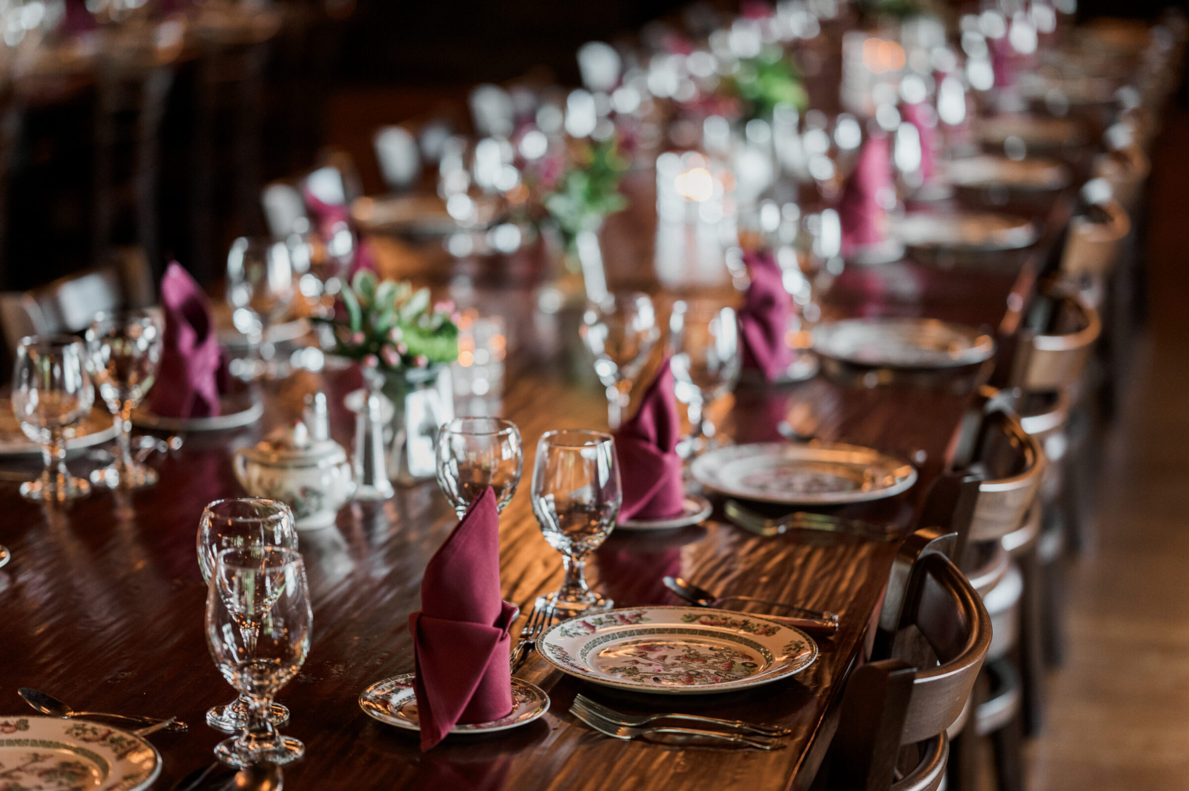 A formal dining table set with ornate plates, wine glasses, and burgundy napkins.