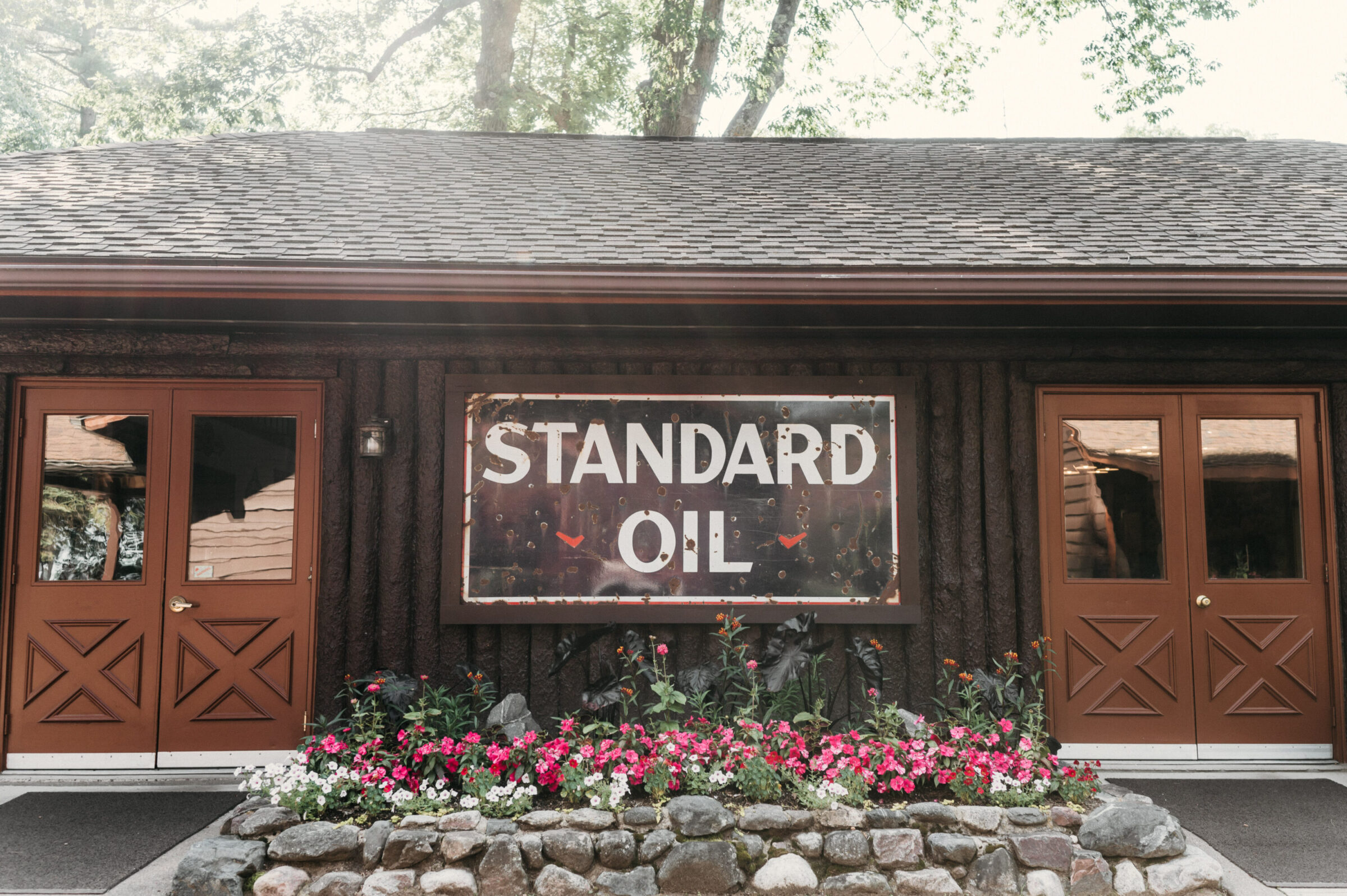 Vintage Standard Oil sign on a rustic building with double doors and flower beds.