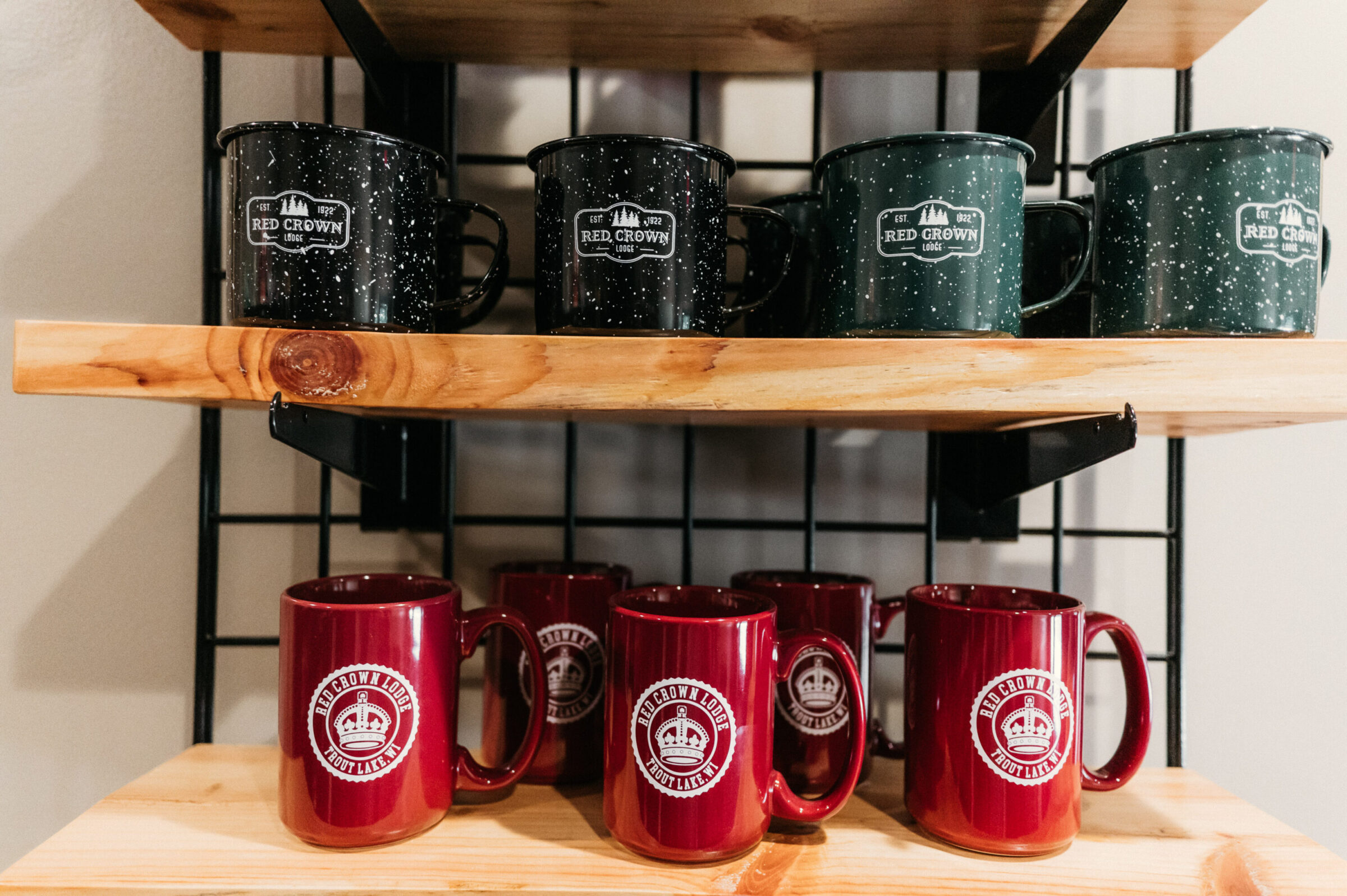 Red Crown Lodge mugs in black, green, and maroon displayed on wooden shelves.