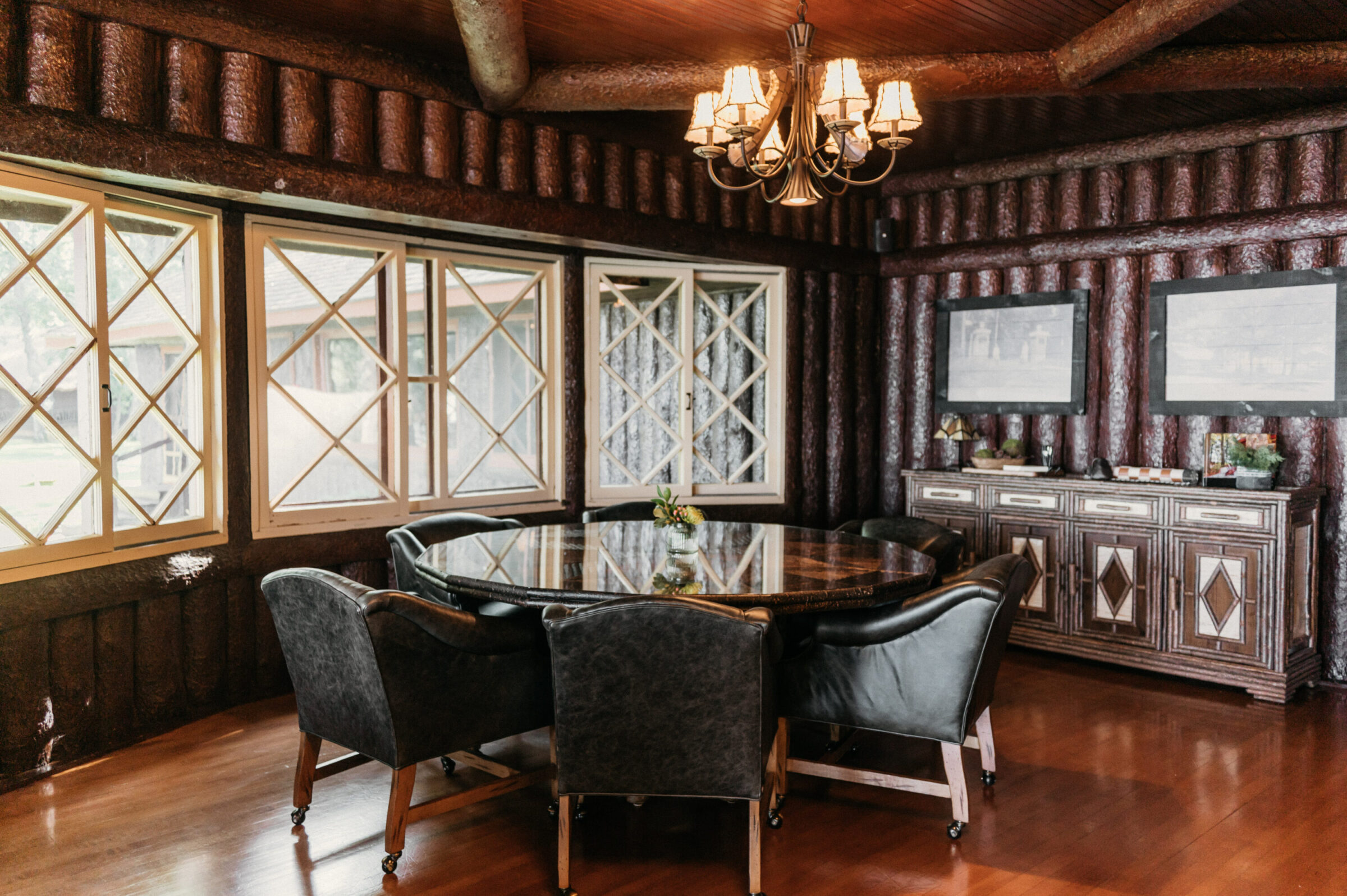Round dining table with leather chairs in a log cabin room with diamond-pane windows.