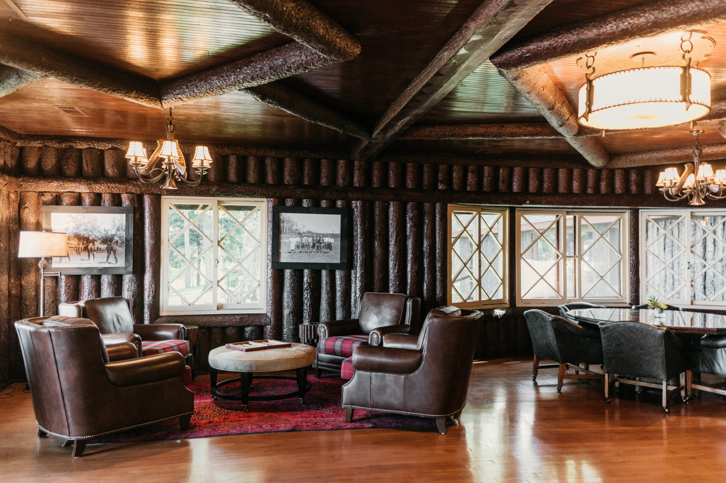 Leather armchairs and a round ottoman in a room with log walls and diamond-paned windows.