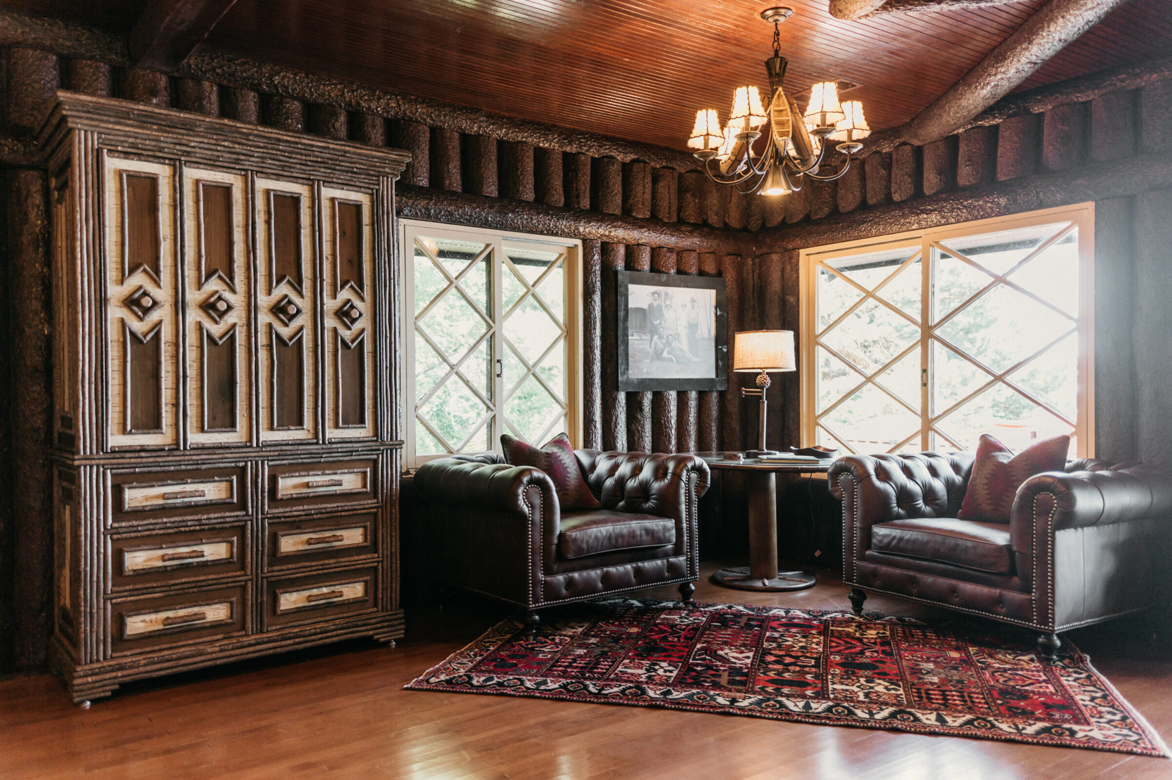 Rustic room with log walls, leather chairs, ornate cabinet, and patterned rug.
