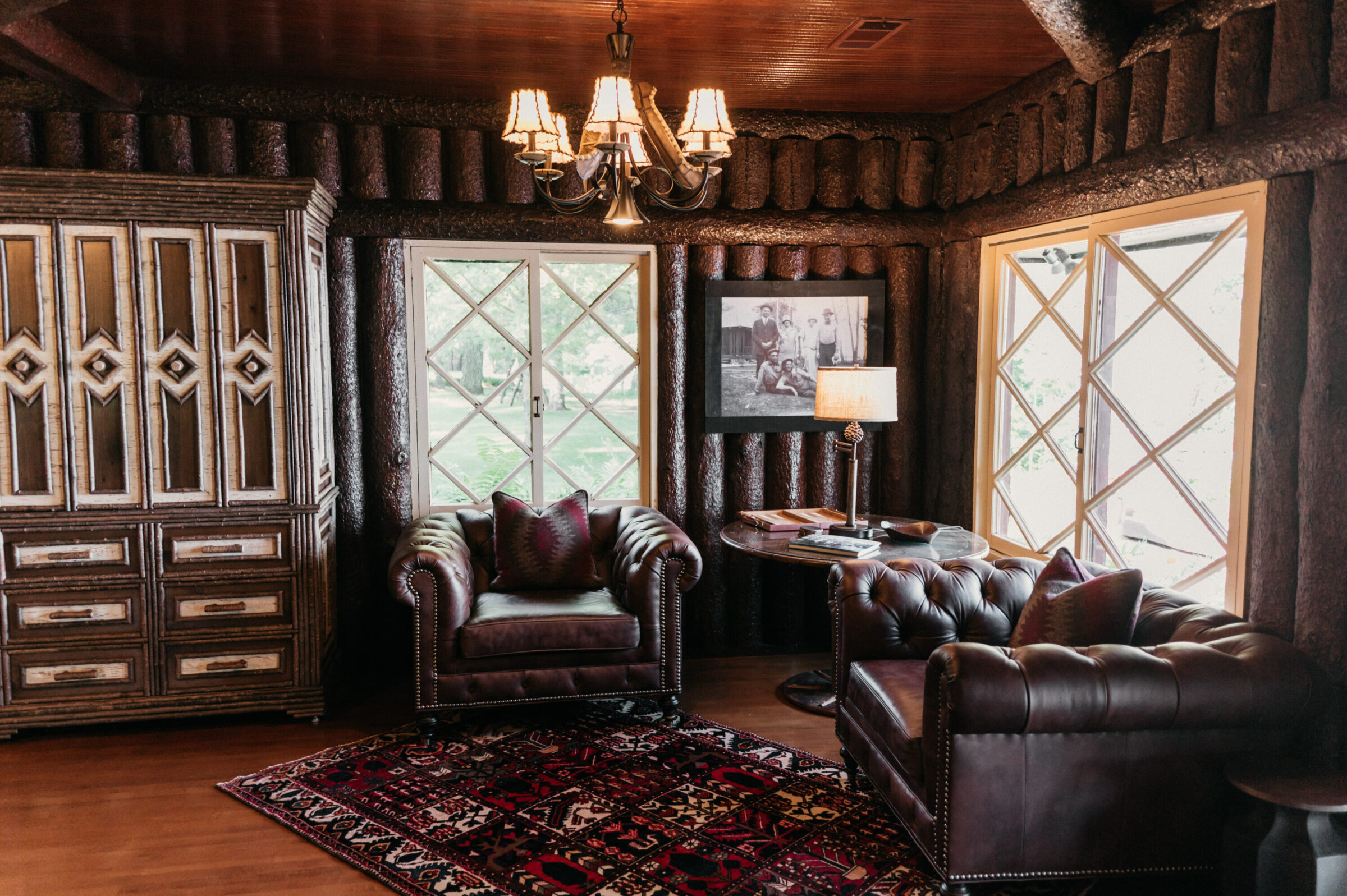 Leather armchairs and ornate cabinet in a rustic room with log walls and diamond-paned windows.