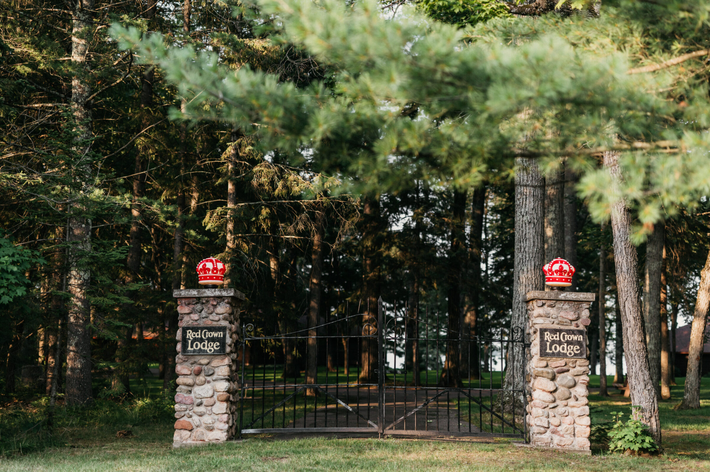 Stone pillars with red crowns and "Red Crown Lodge" signs flank a black metal gate.