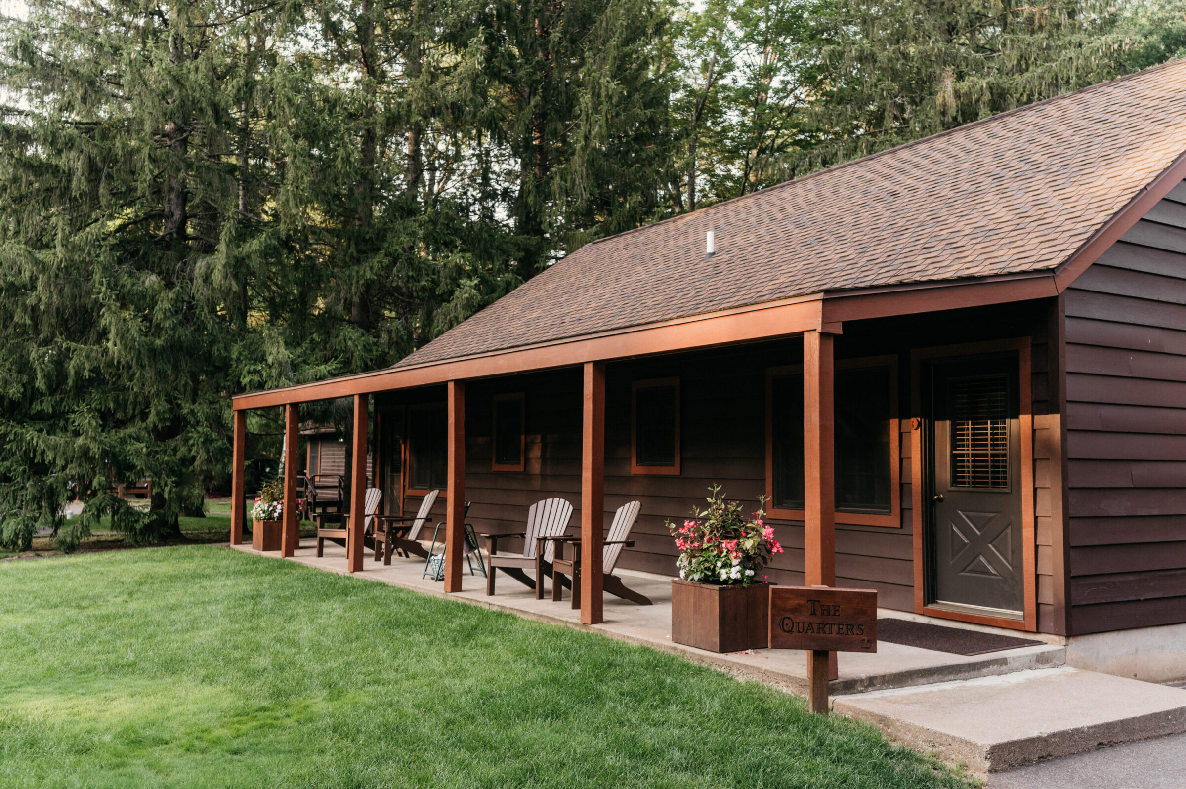Brown cabin with a covered porch, Adirondack chairs, and a sign reading "The Quarters".
