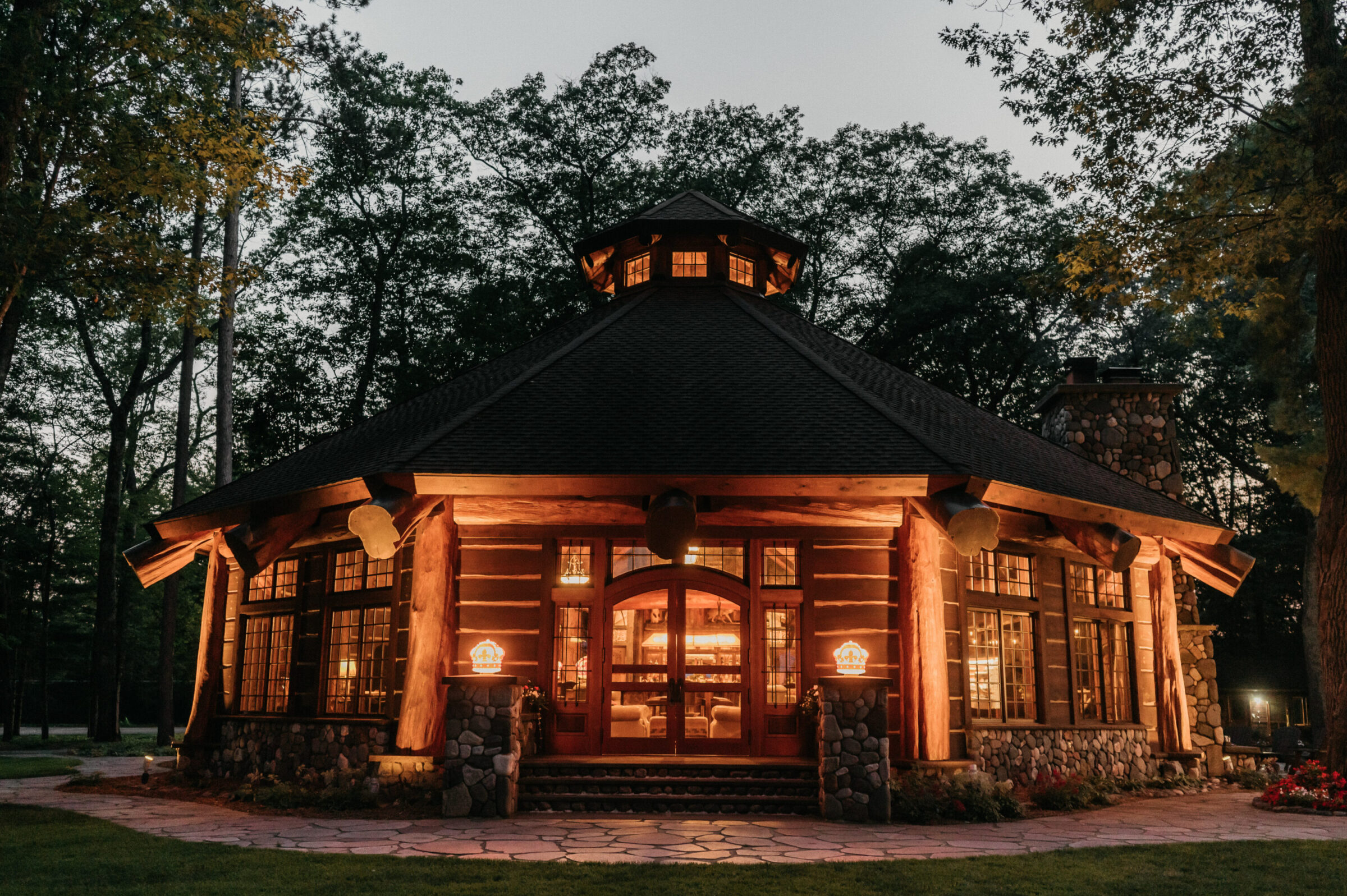 Round log cabin with stone accents and warm interior lighting at dusk.