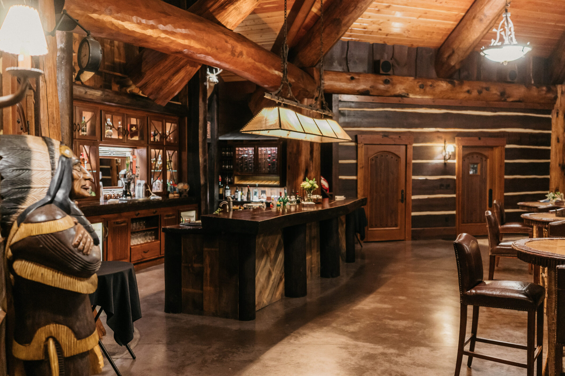 Log cabin bar with wooden beams, a large bar, and Native American statue.