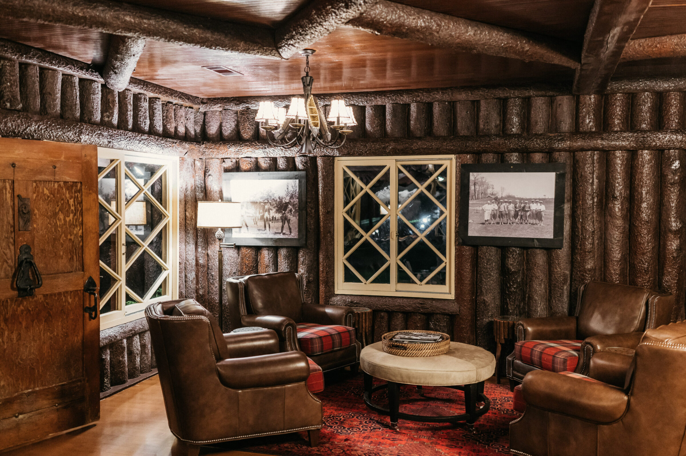 Cozy log cabin living room with leather chairs and plaid cushions.