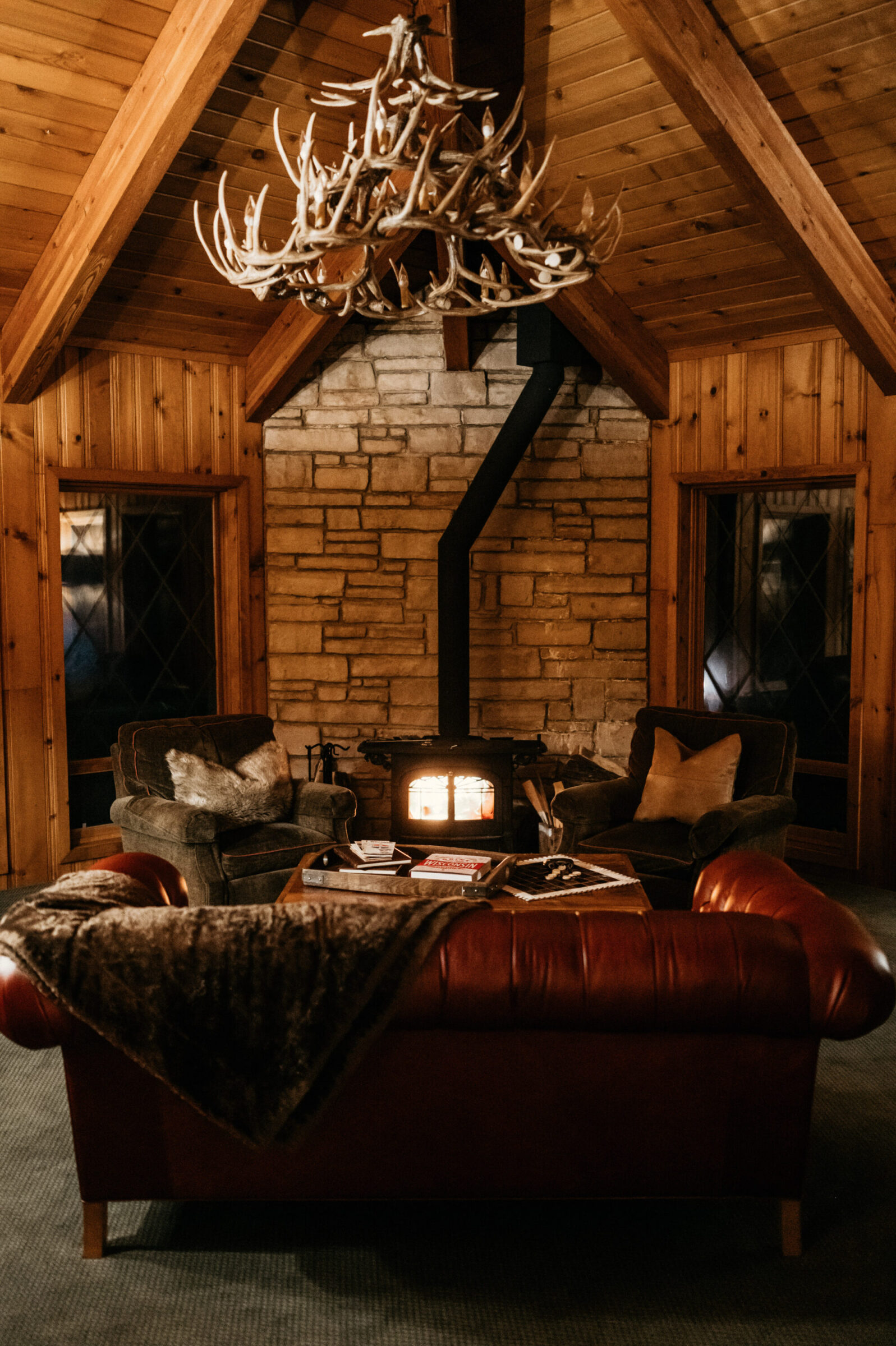Cozy living room with fireplace, antler chandelier, and leather sofa.